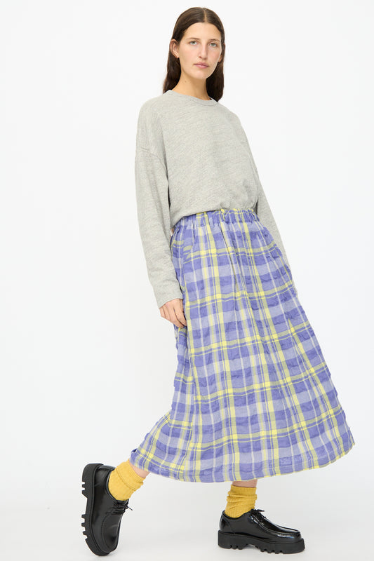 A person stands against a white background wearing a gray long-sleeve top, yellow socks, black platform shoes, and the Ichi Antiquités Cotton Wool Tartan Check Skirt in Blue.