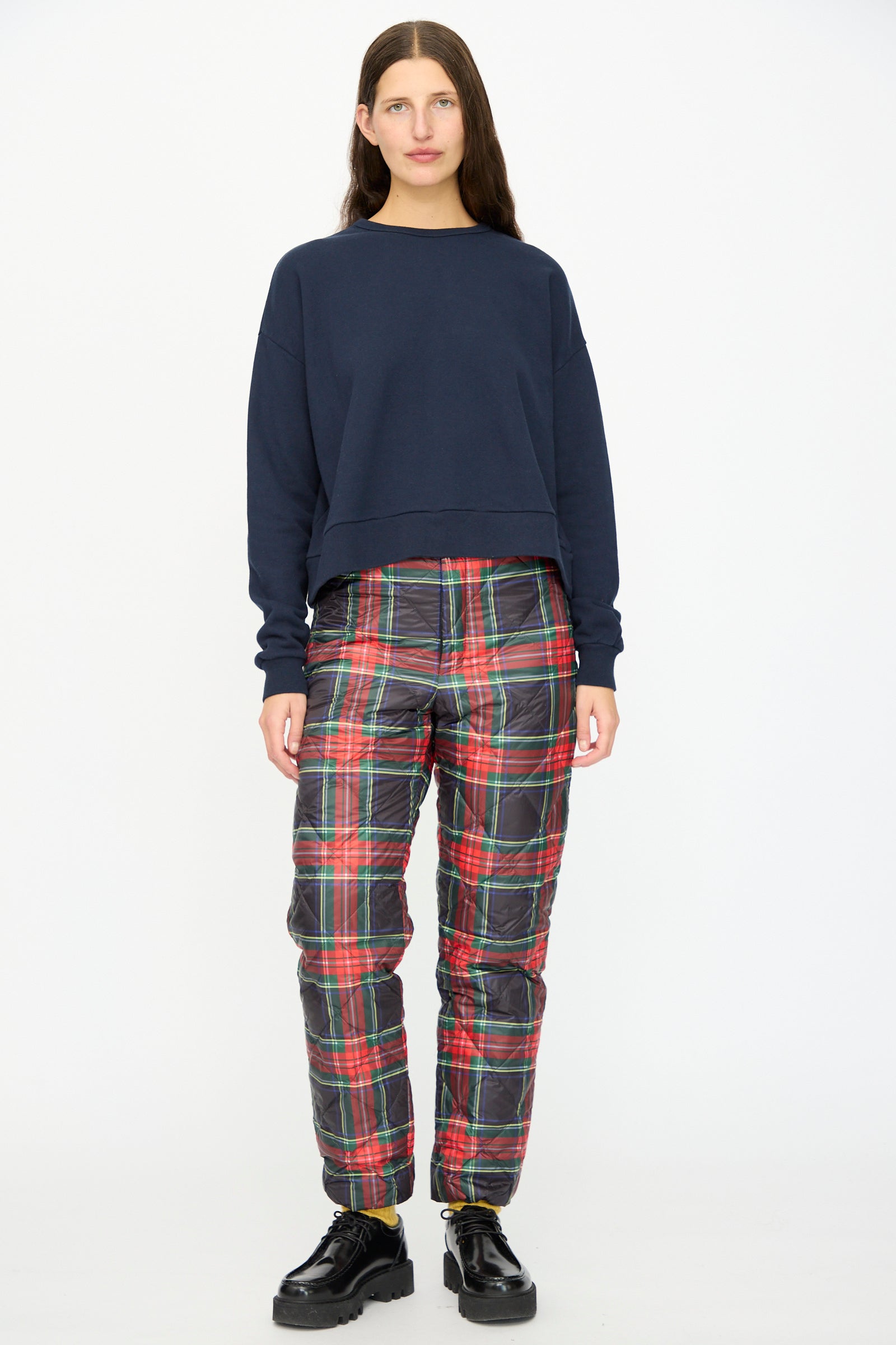 A person stands facing forward against a plain white background, wearing an Ichi Antiquités navy sweatshirt, Down Pants in Black Tartan with an elastic waist, and black platform shoes.