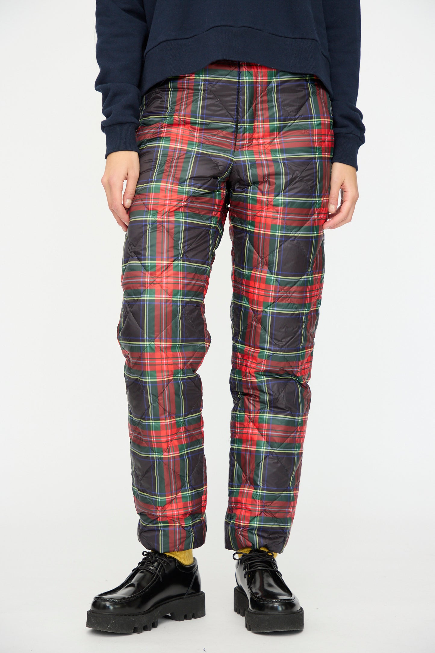 A person wears Ichi Antiquités Down Pants in Black Tartan with an elastic waist, a navy sweatshirt, yellow socks, and black platform shoes, standing against a plain white background.