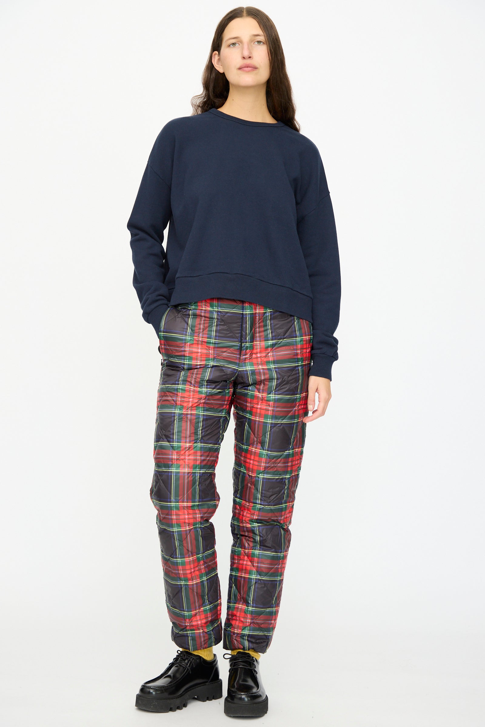 A person faces forward against a plain white background, wearing a navy sweatshirt, black shoes, and Ichi Antiquités Down Pants in Black Tartan featuring an elastic waist and quilted design.