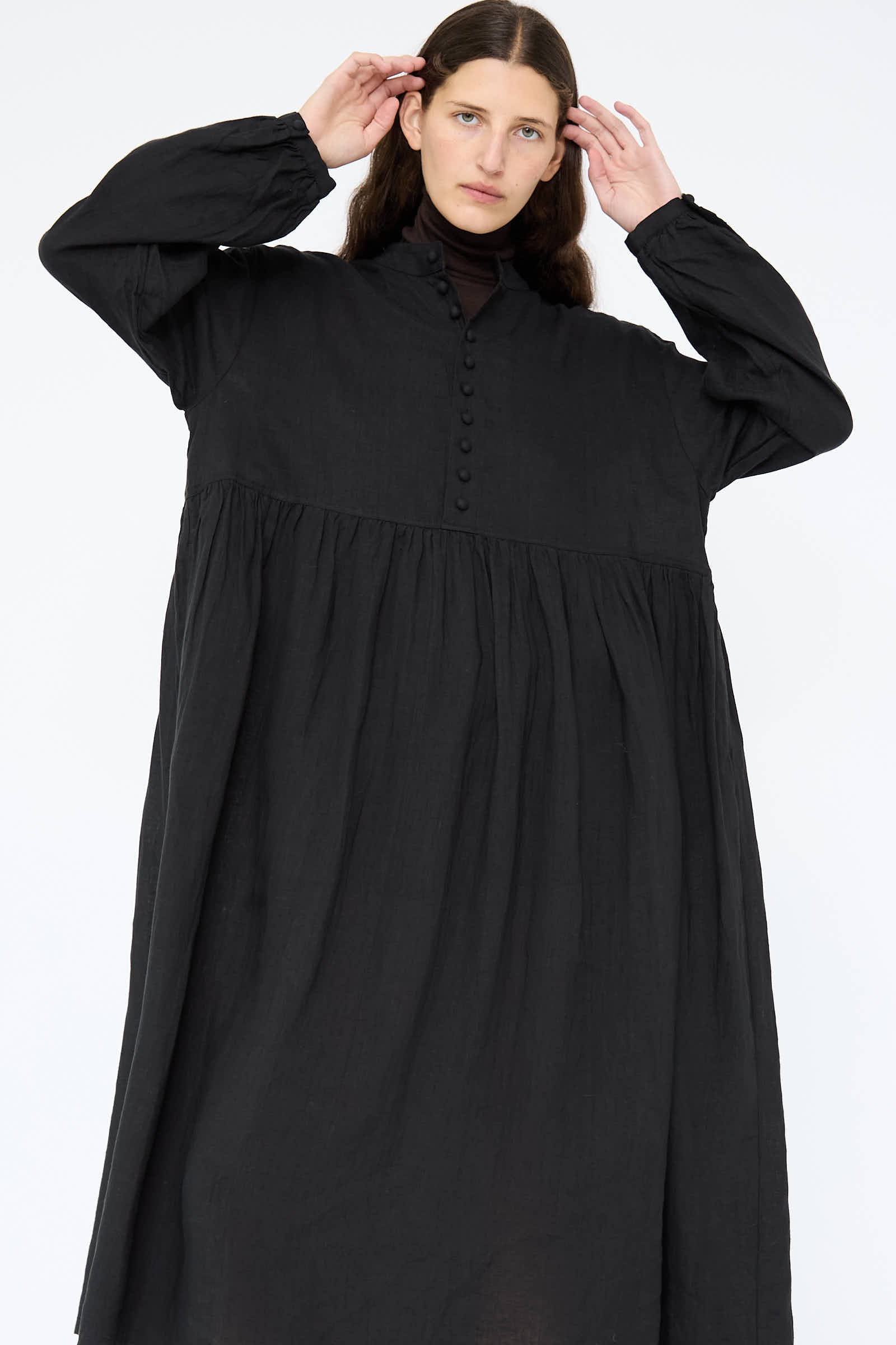 A person is clad in the French Linen Dress in Black by Ichi Antiquités, featuring a relaxed fit with long sleeves and a high collar, standing against a plain background.