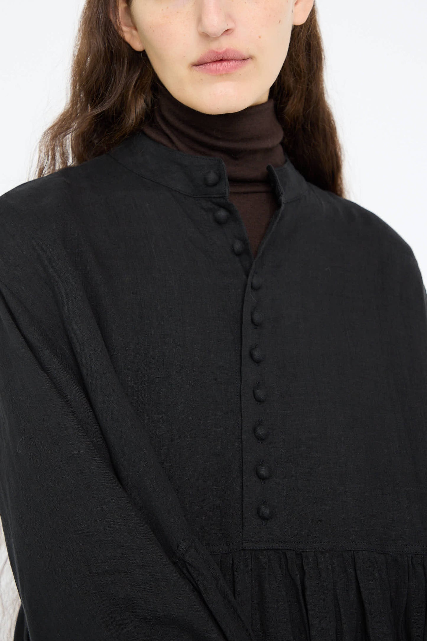 A person is wearing the French Linen Dress in Black by Ichi Antiquités, styled with a relaxed-fit brown turtleneck underneath.