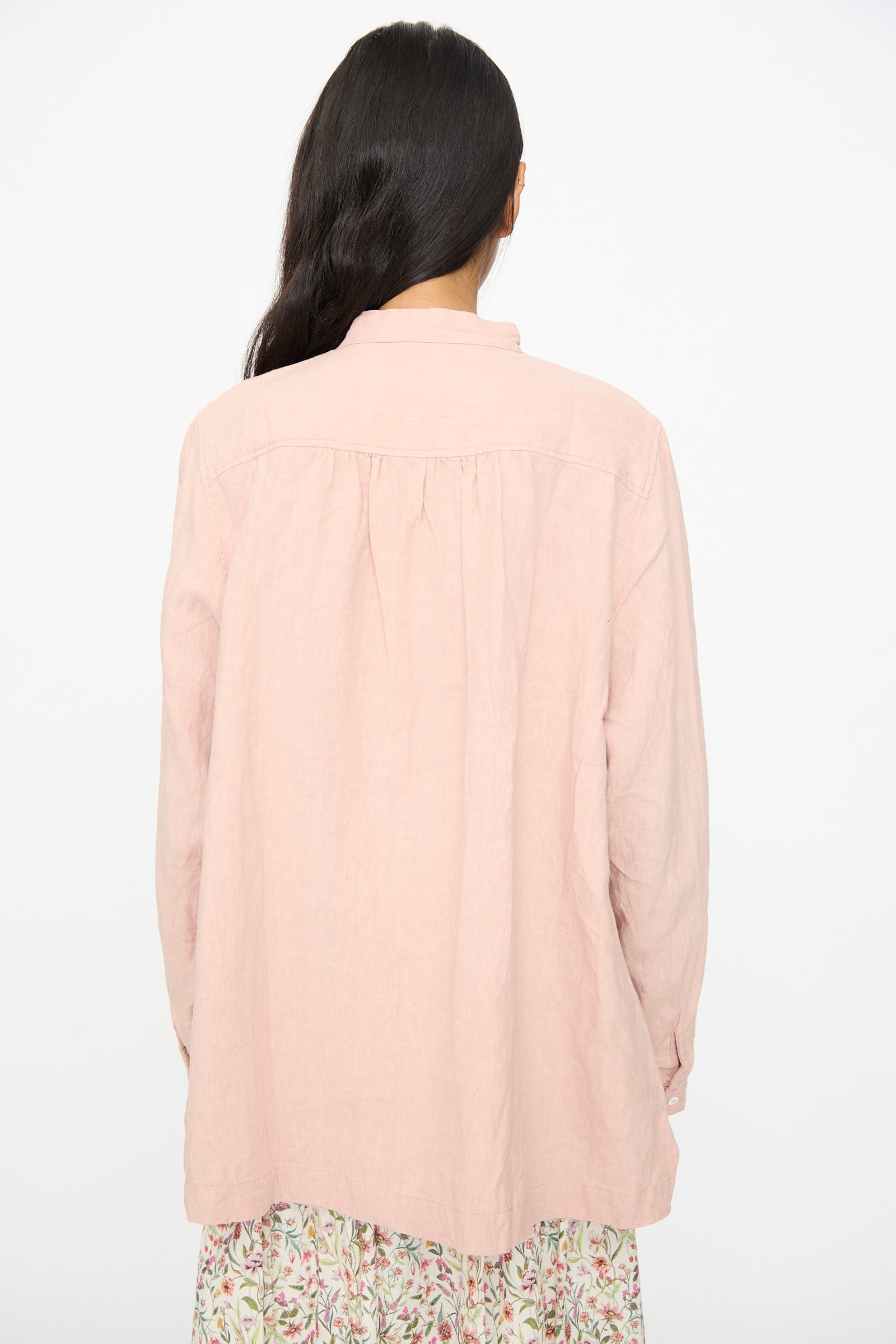 A woman with long dark hair, seen from behind, wears the French Linen Shirt in Pink by Ichi Antiquités over a floral-patterned skirt against a plain white background.