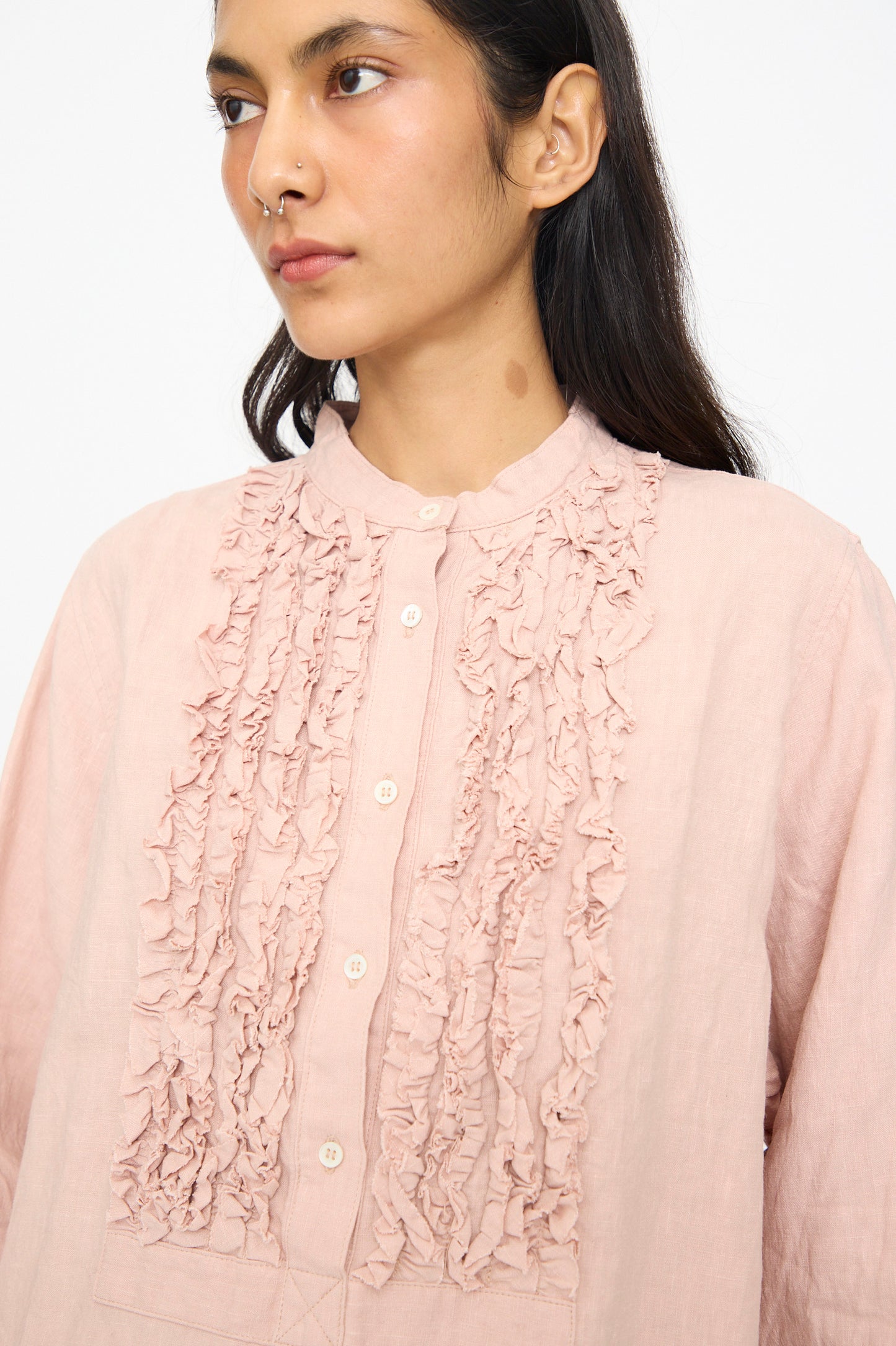 A person wearing the Ichi Antiquités French Linen Shirt in Pink, featuring long sleeves, ruffle detail, and a band collar, shown from the chest up against a plain background.