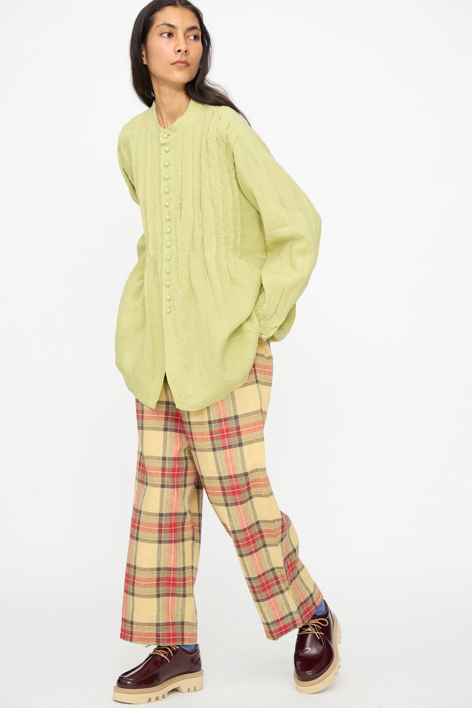 A woman wears the Ichi Antiquités French Linen Shirt in Pistachio with yellow plaid pants and burgundy loafers, standing against a plain white background.