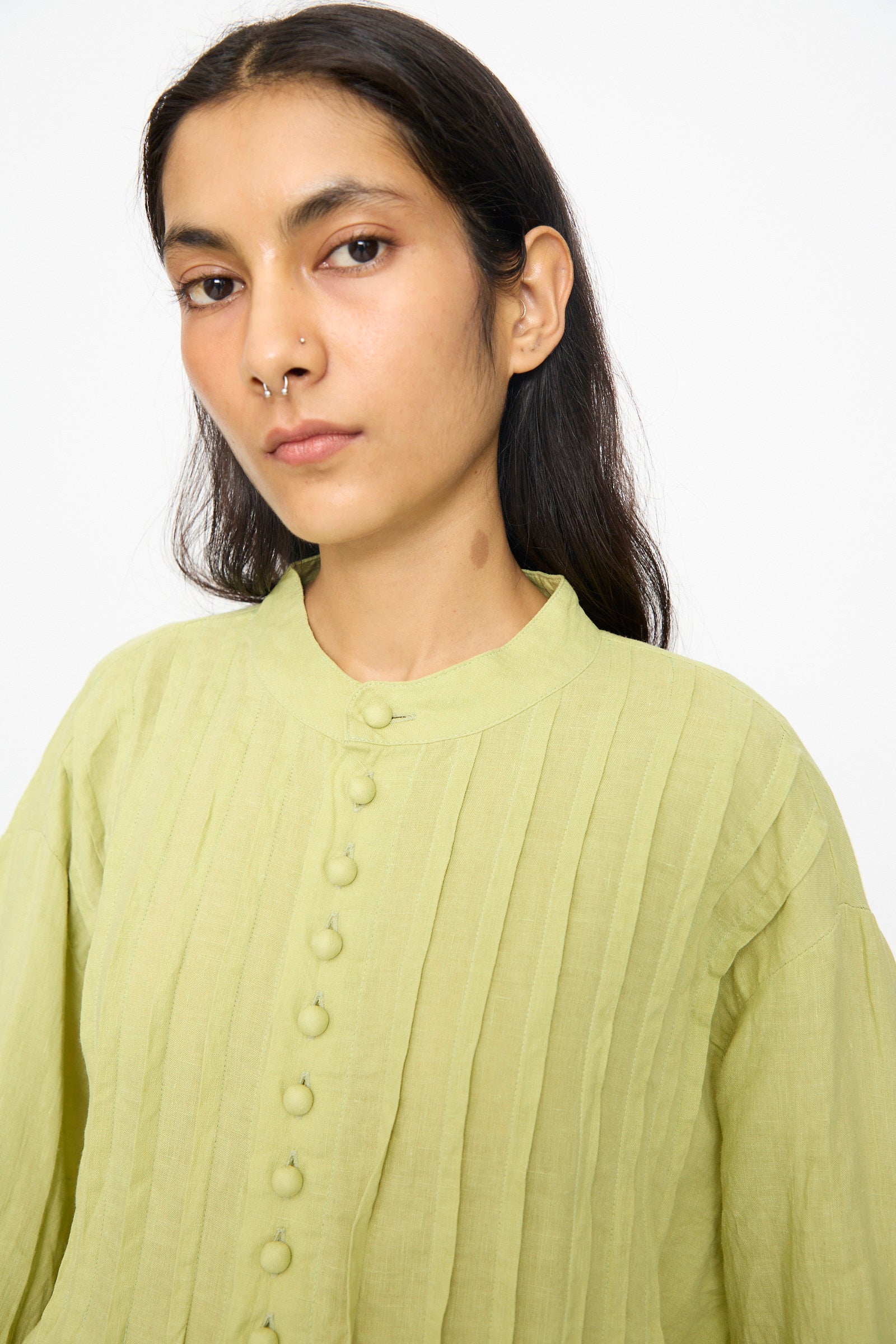 A person with long dark hair wears the Ichi Antiquités French Linen Shirt in Pistachio, featuring a band collar and textured fabric, while looking at the camera against a plain white background.