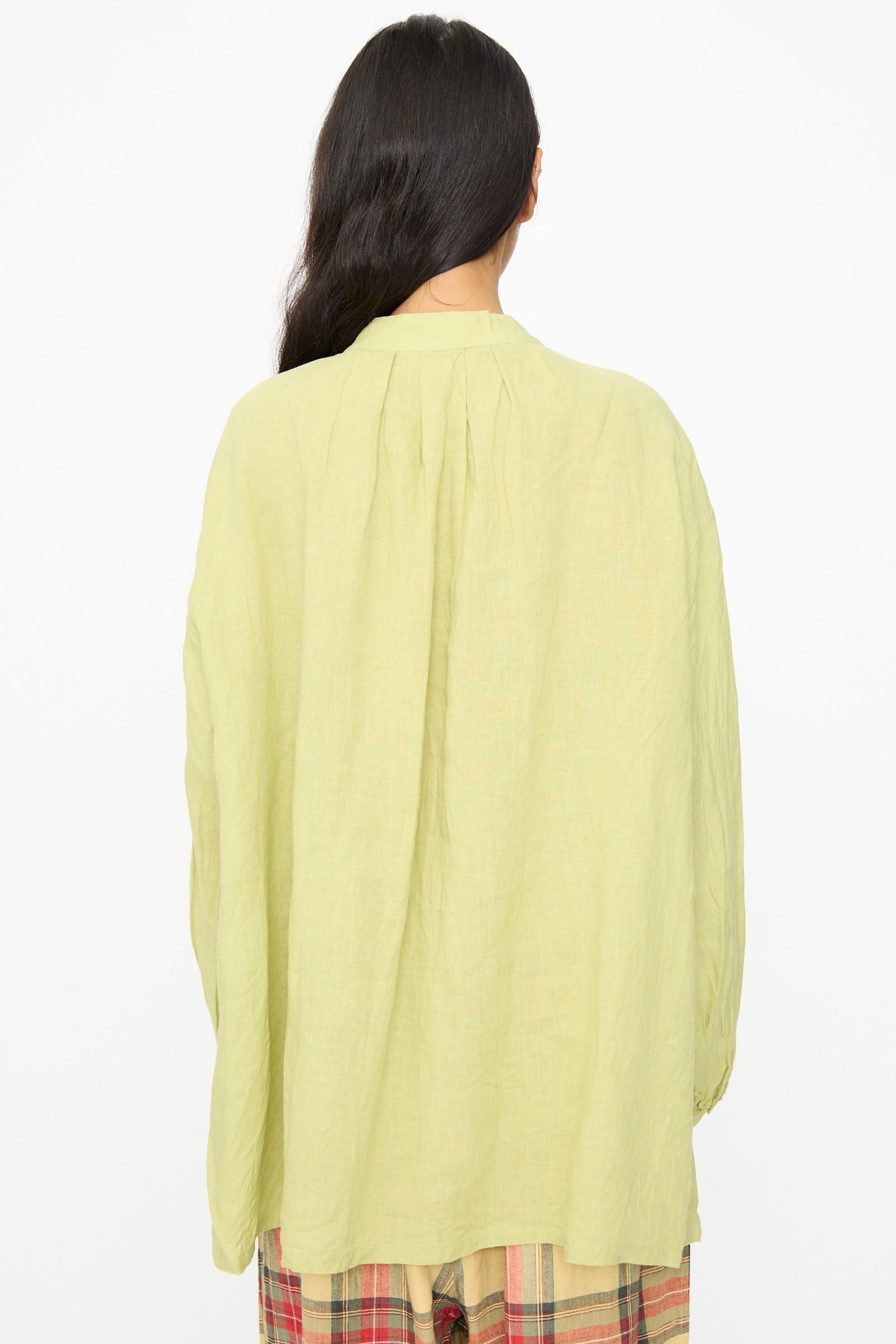 A person with long dark hair is shown from the back, wearing the Ichi Antiquités French Linen Shirt in Pistachio, featuring a loose fit and band collar, paired with plaid pants against a plain white background.