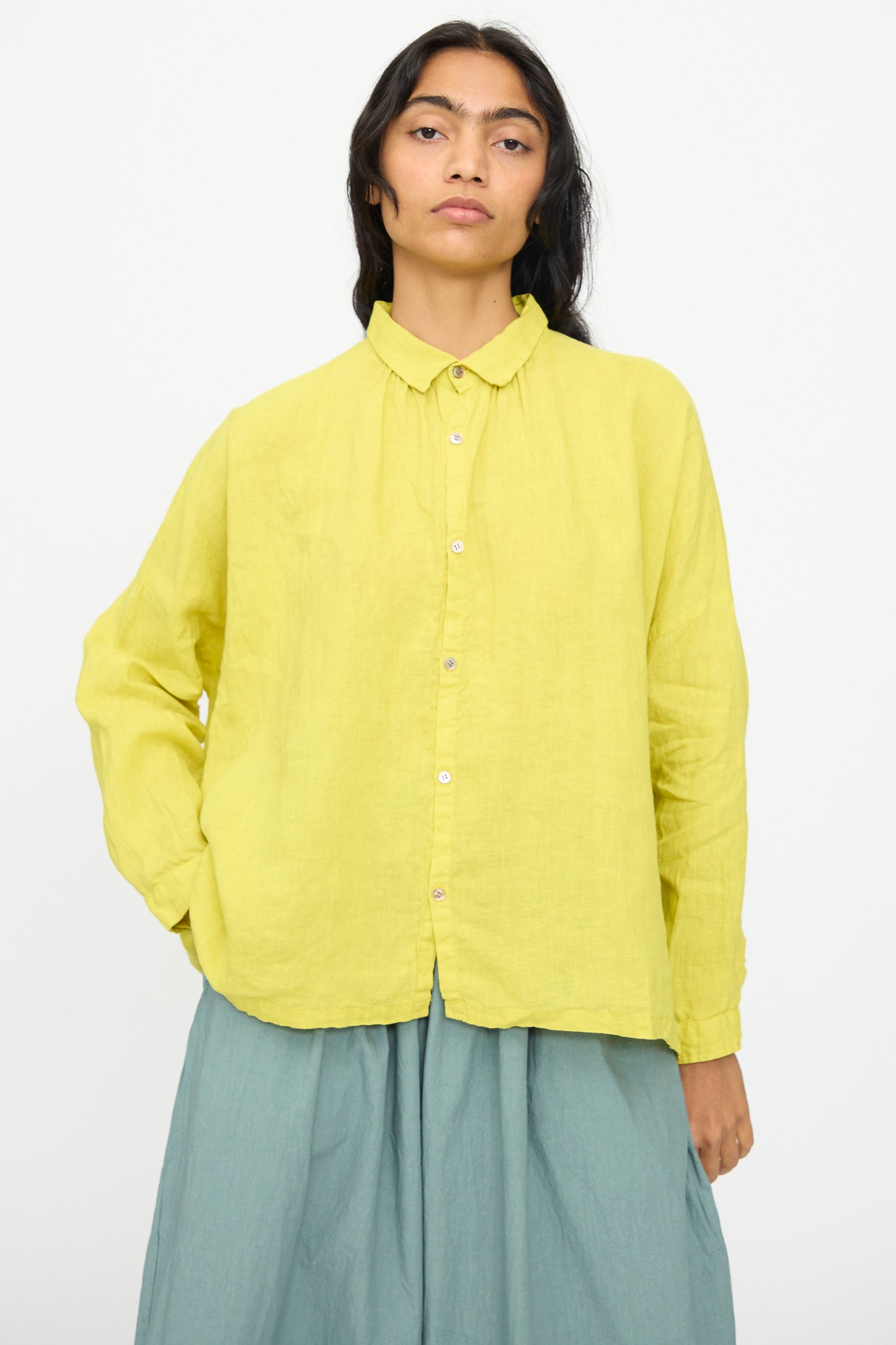 A person with long dark hair wears the Ichi Antiquités French Linen Shirt in Yellow, paired with a light blue skirt, standing against a plain white background.