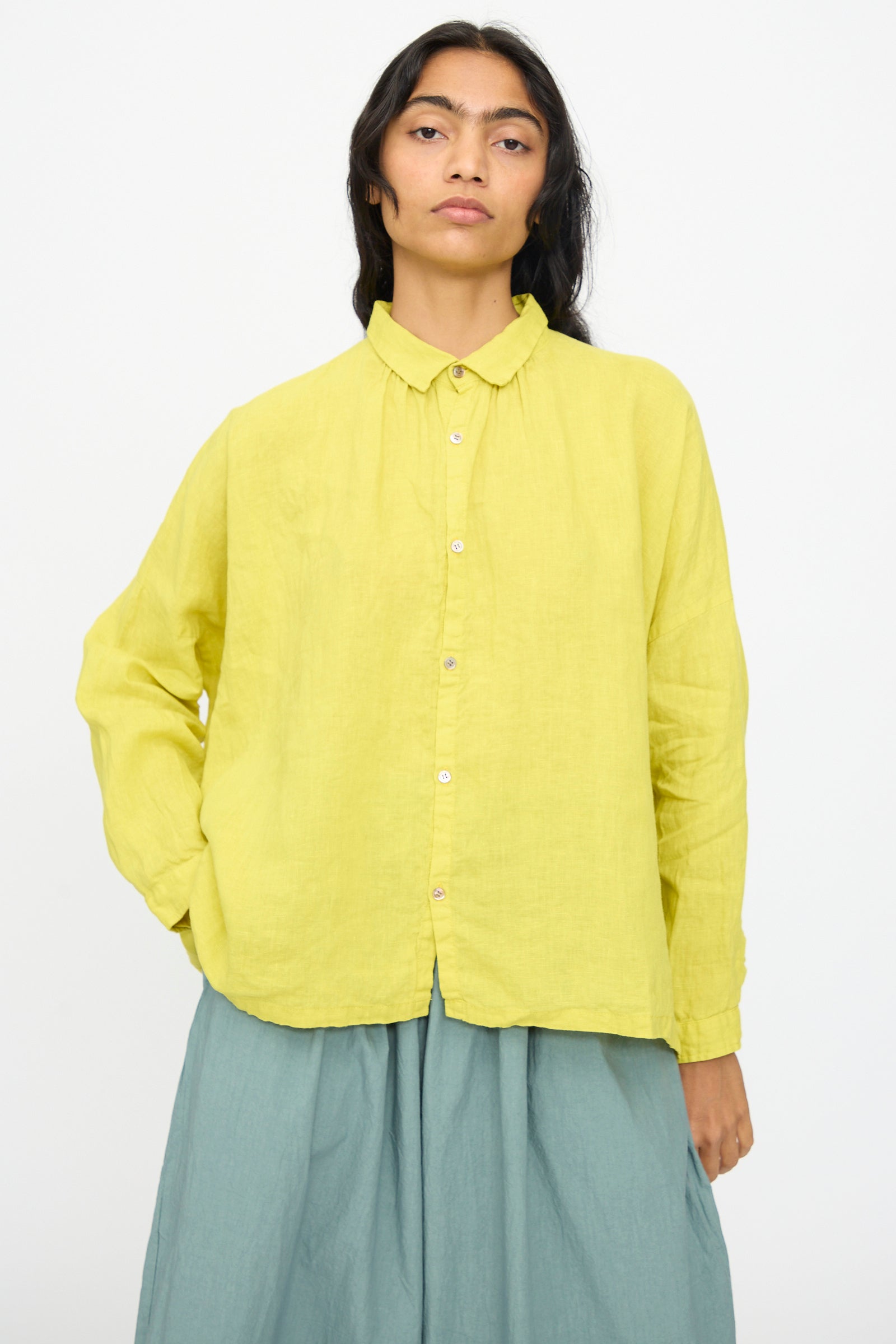 A person with long dark hair wears the Ichi Antiquités French Linen Shirt in Yellow, paired with a light blue skirt, standing against a plain white background.