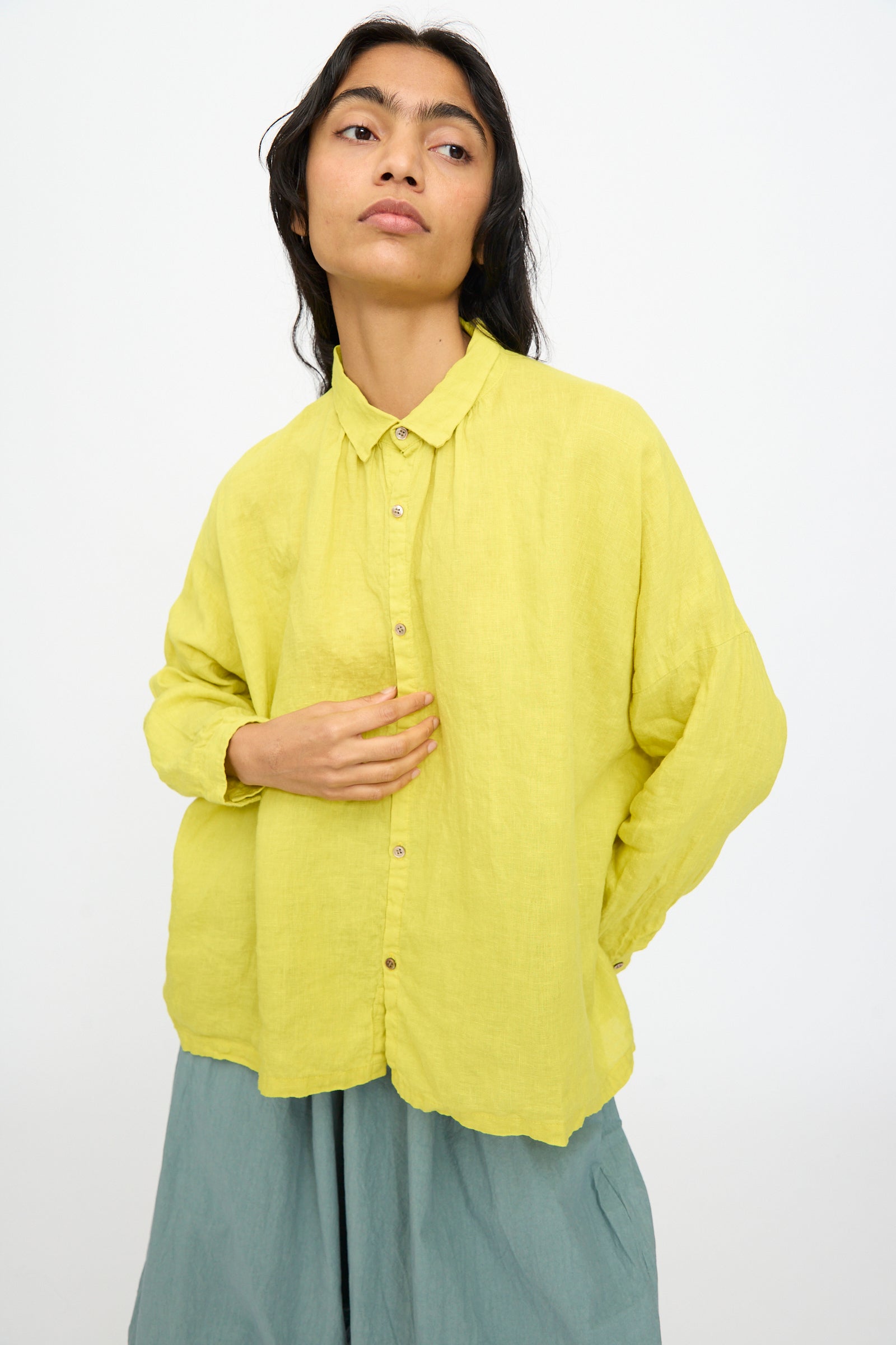 A person wears Ichi Antiquités’ French Linen Shirt in Yellow with a light blue skirt, standing against a plain white background.