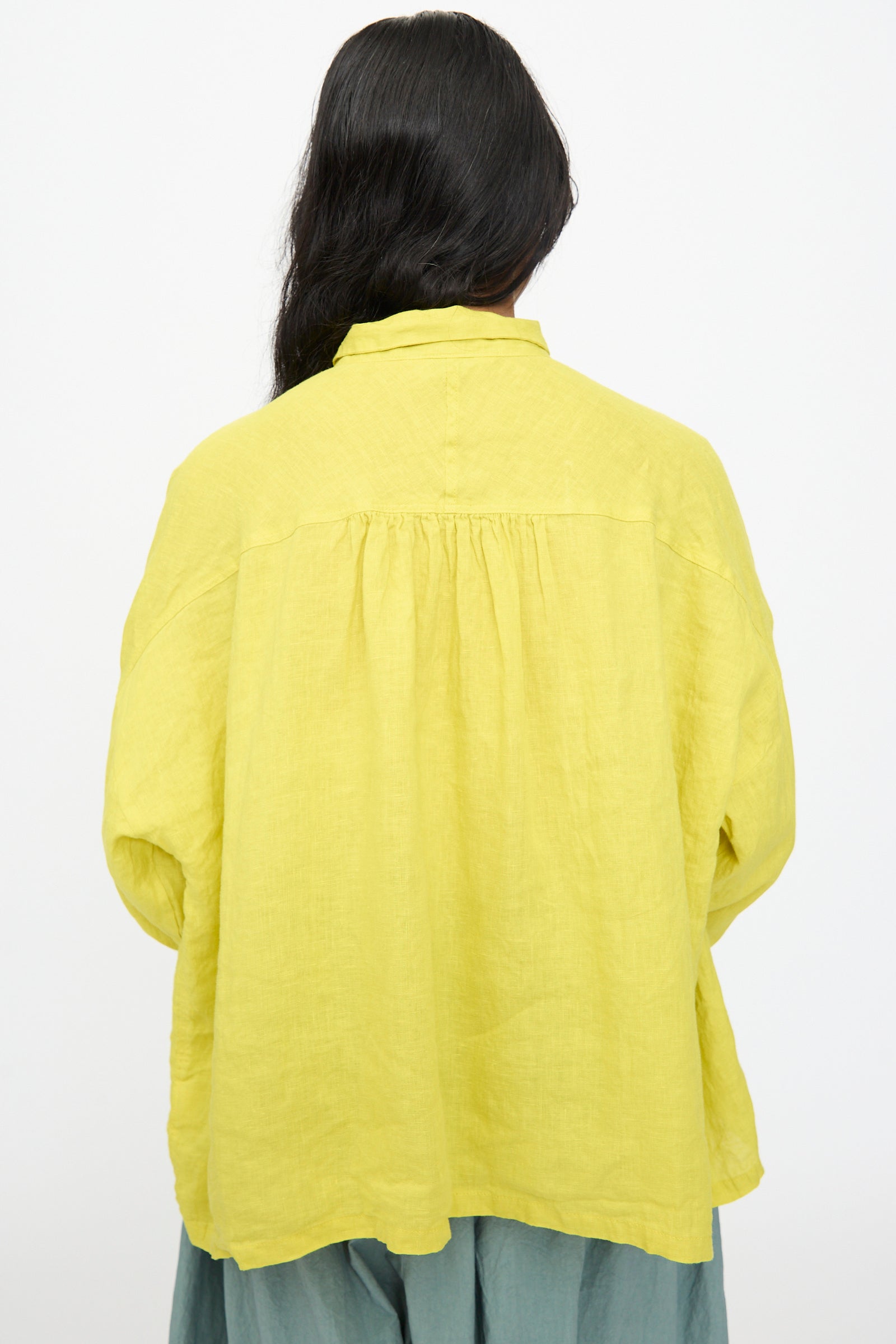 A person with long dark hair is seen from the back, wearing the Ichi Antiquités French Linen Shirt in Yellow and green pants, set against a plain white background.