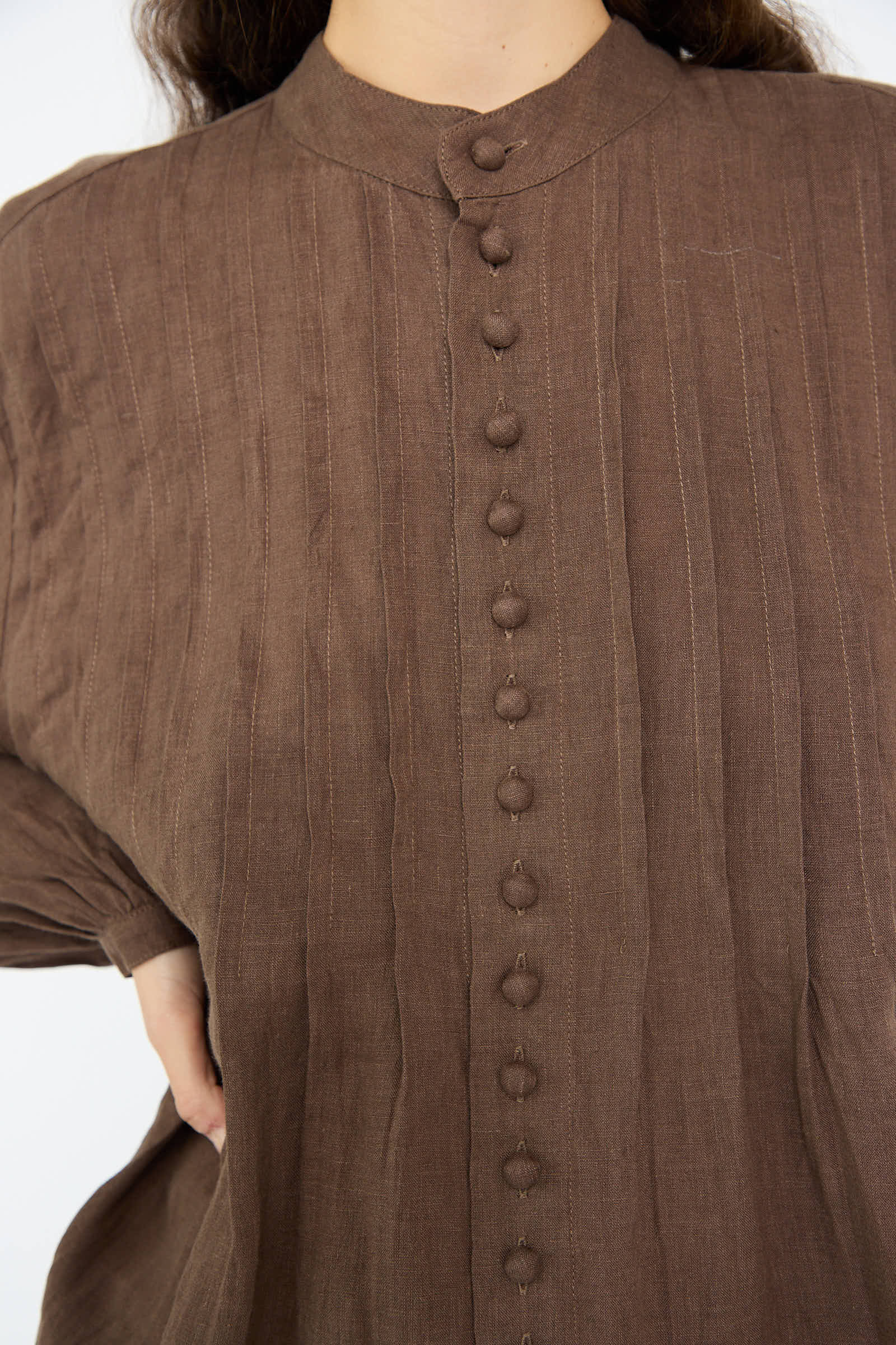 Close-up of a person wearing the Ichi Antiquités French Linen Shirt in Brown, featuring a textured design with a band collar and long sleeves, set against a white background.