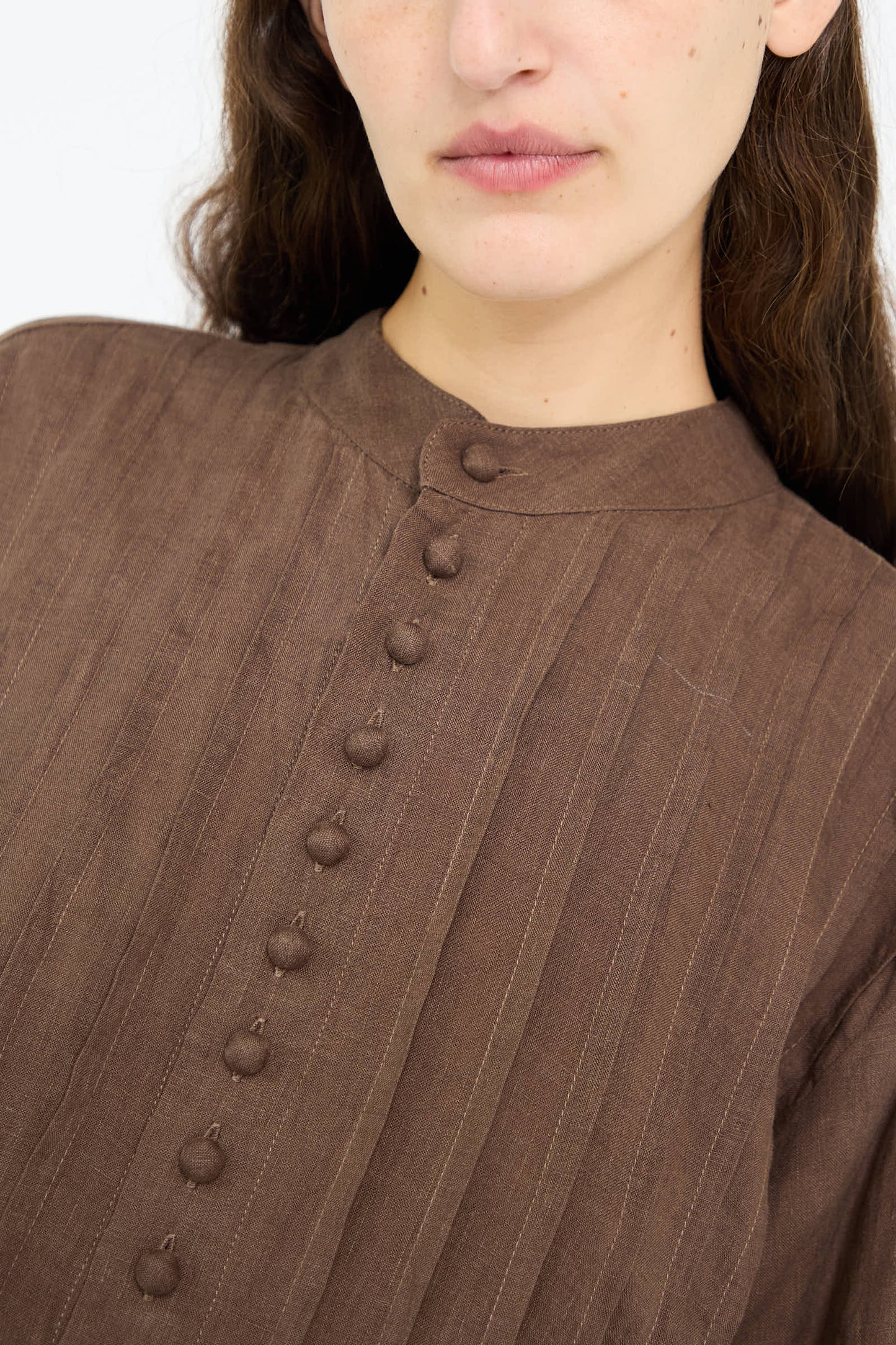 Close-up of a person wearing the French Linen Shirt in Brown by Ichi Antiquités, showcasing its textured fabric and relaxed fit, along with a distinctive band collar.