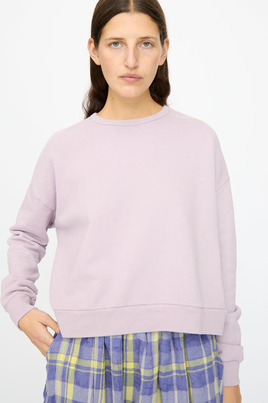 A person with long brown hair models the Ichi Antiquités French Terry Cotton Pullover in Lavender, paired with a blue and yellow plaid skirt, against a plain white background.