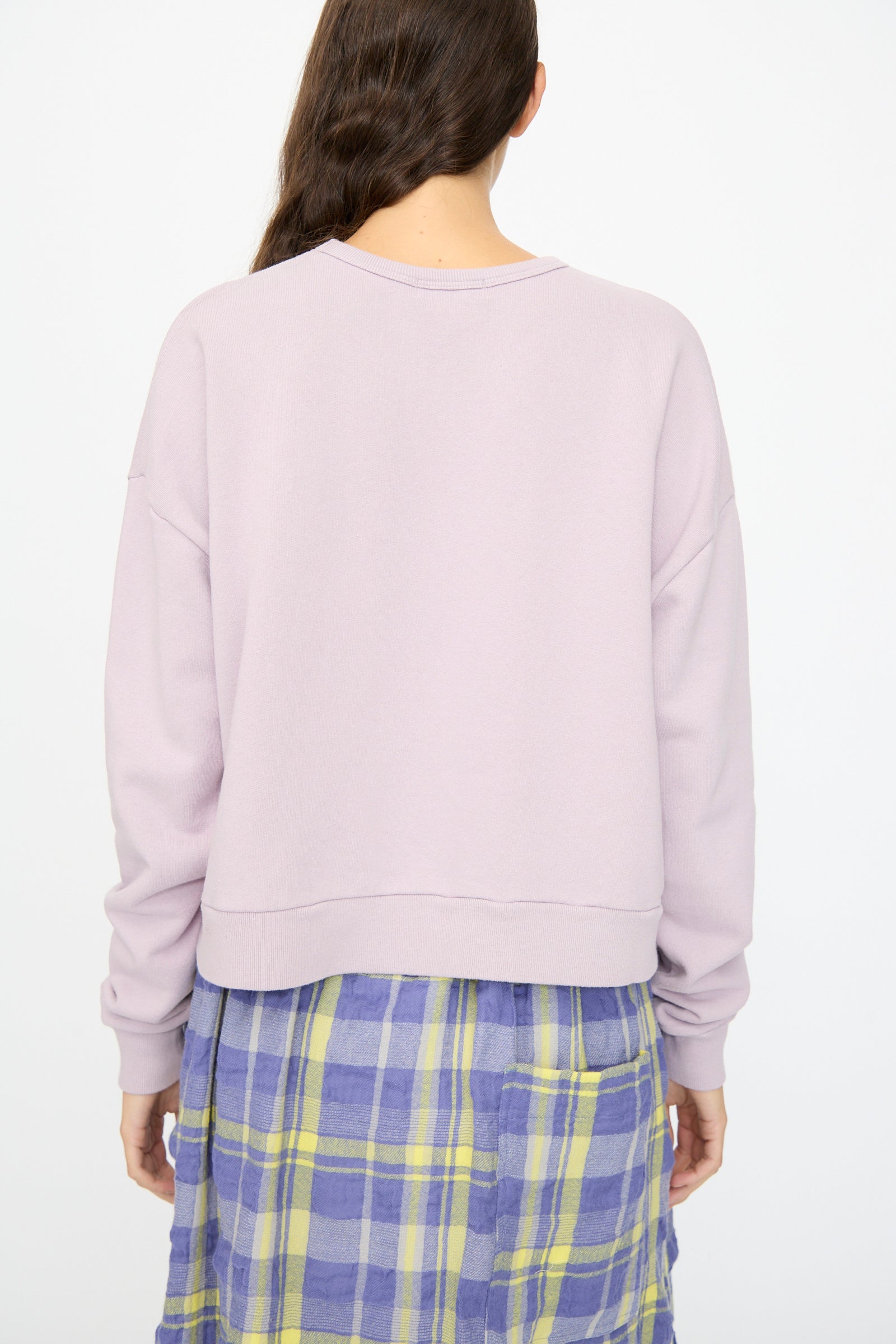 A person with long brown hair is shown from the back, wearing the Ichi Antiquités French Terry Cotton Pullover in Lavender and a blue and yellow plaid skirt.
