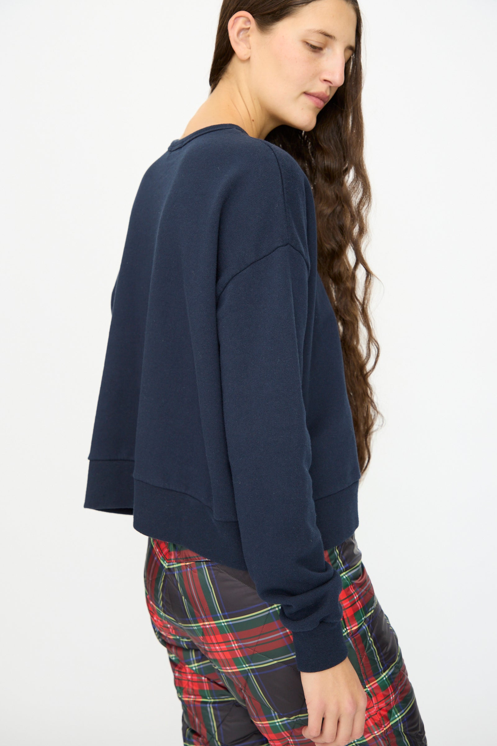 A woman with long brown hair models the Ichi Antiquités French Terry Cotton Pullover in Navy and plaid pants, standing sideways against a plain white background.