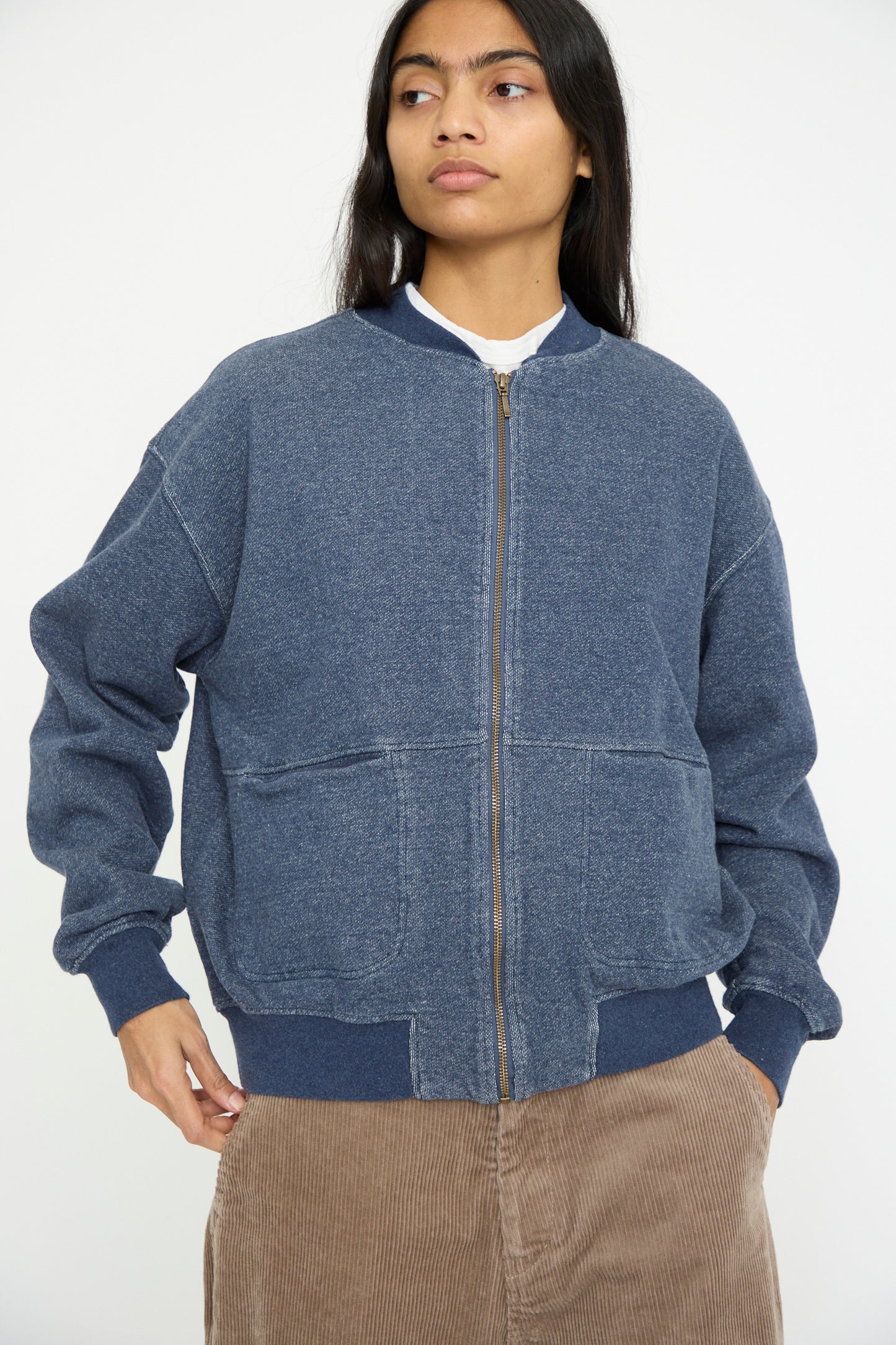 A person stands against a plain background, wearing the Ichi Antiquités French Terry Denim Blouson in Navy—a relaxed-fit zip-up jacket—paired with brown corduroy pants.