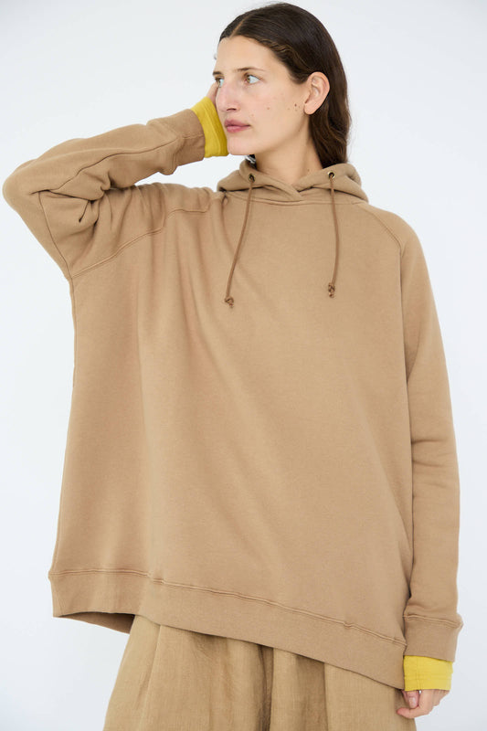 The individual is dressed in the French Terry Hoodie in Beige by Ichi Antiquités, featuring an oversized fit and crafted from quality French terry cotton. A vibrant yellow inner layer adds a pop of color, as they stand confidently against a plain backdrop, seamlessly combining comfort and style.