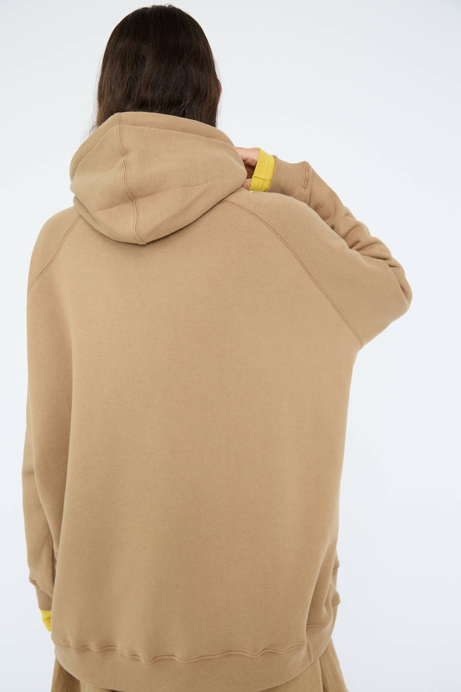 A person with long hair is wearing the oversized French Terry Hoodie in Beige from Ichi Antiquités, the hood pulled up, facing away.