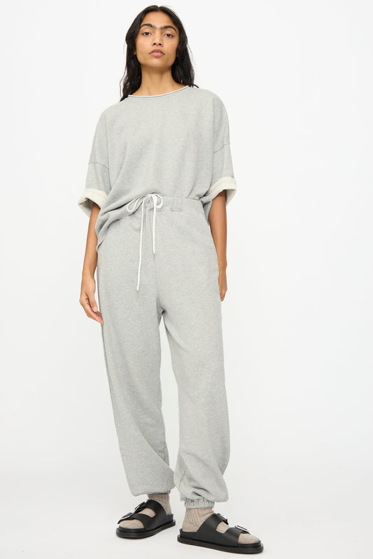 A person stands against a white background wearing Ichi Antiquités French Terry Pants in Gray, a loose grey sweatshirt, and black sandals with socks.