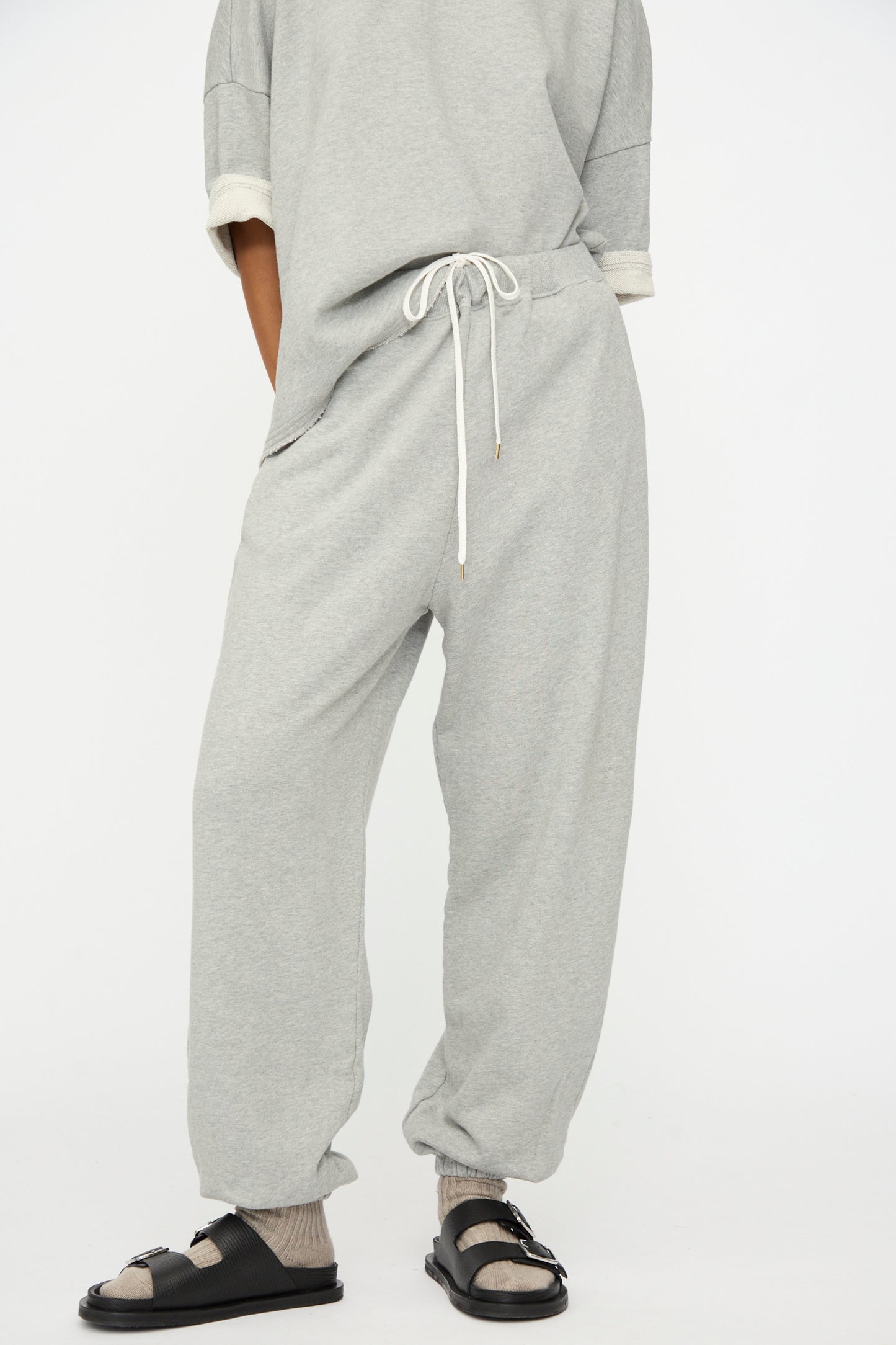 A person wears Ichi Antiquités French Terry Pants in Gray with a matching top, socks, and black sandals, standing against a plain white background.