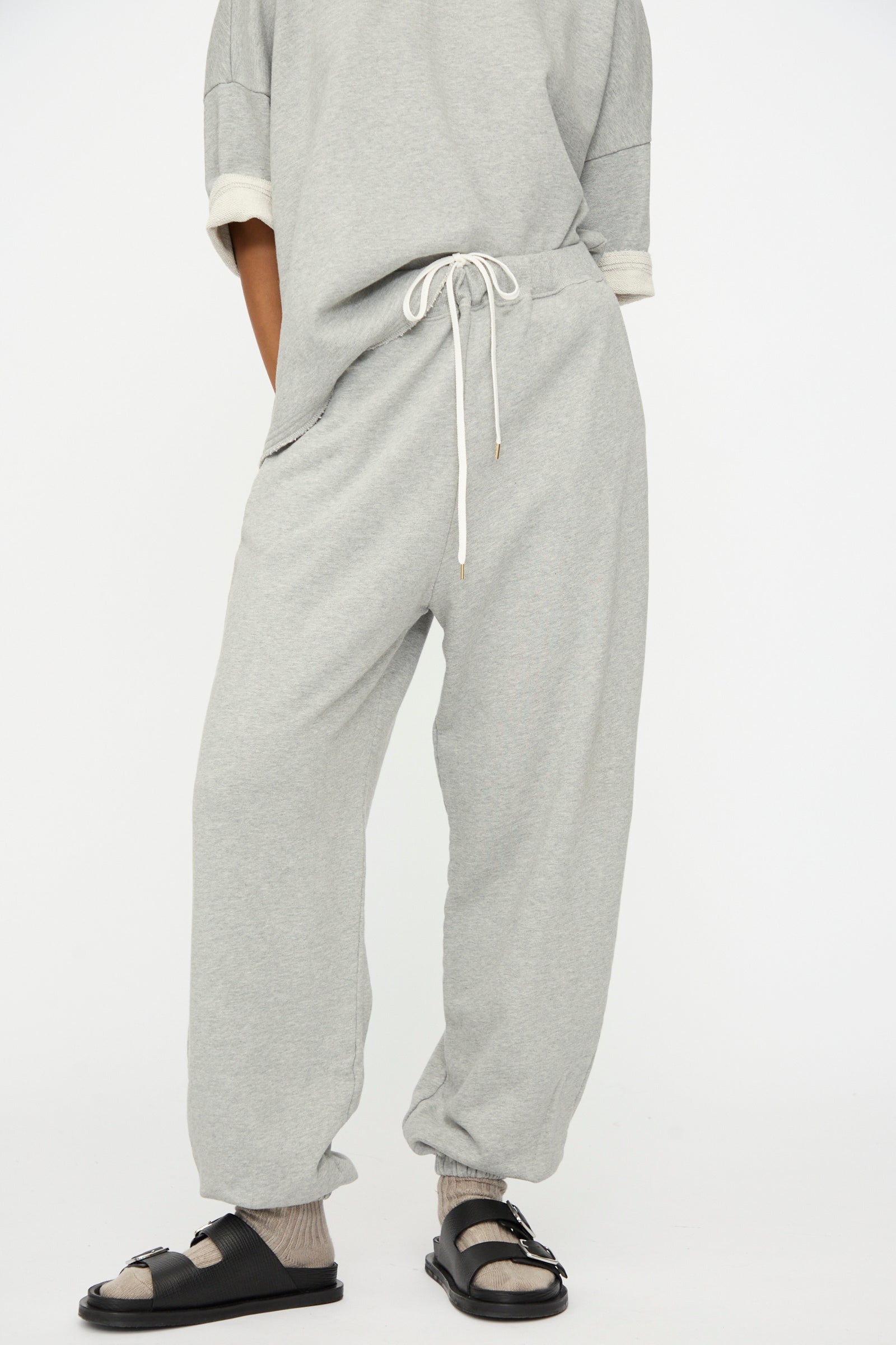 A person wears Ichi Antiquités French Terry Pants in Gray with a matching top, socks, and black sandals, standing against a plain white background.