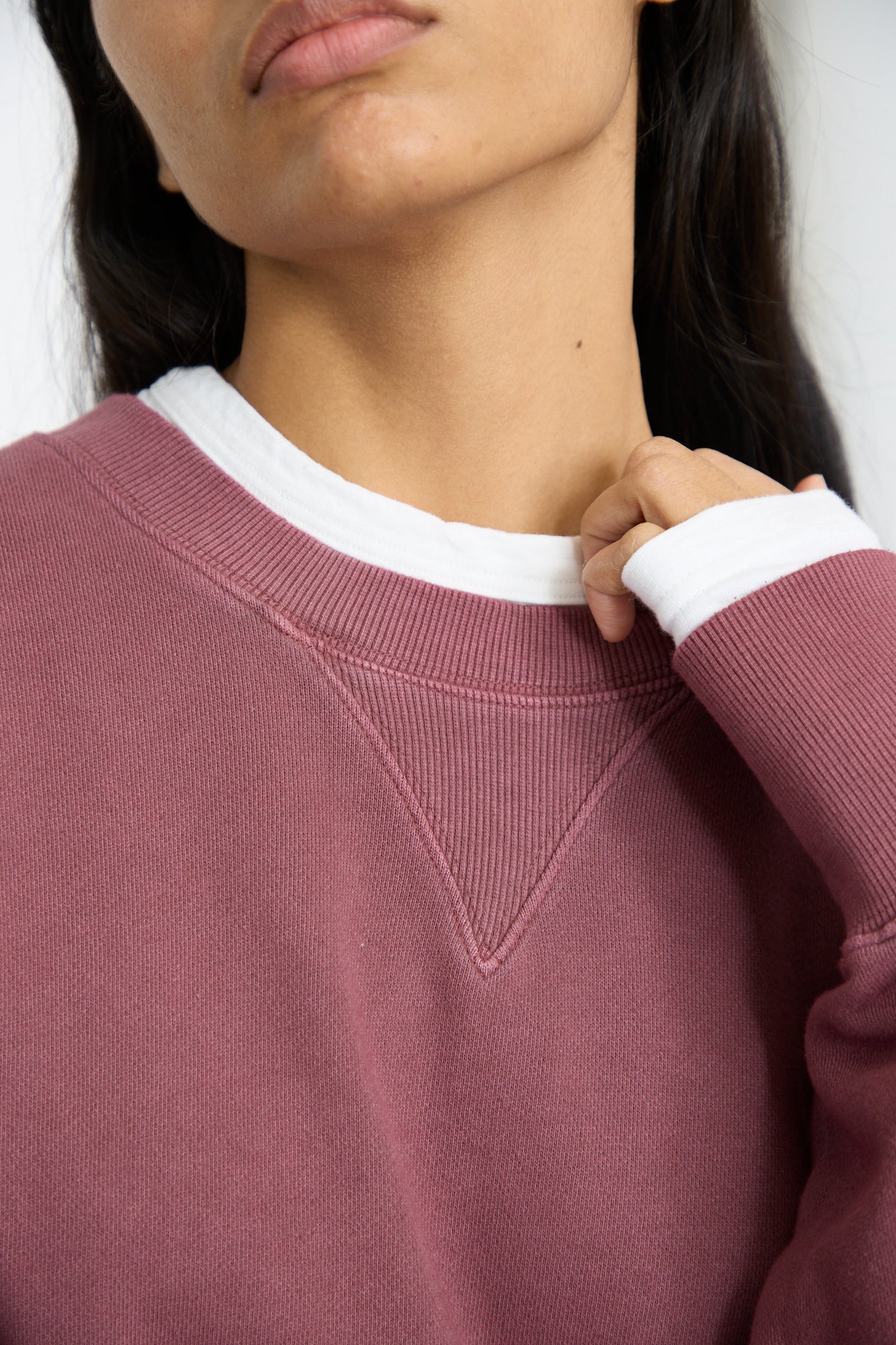 A close up of a person wearing an oversized Ichi Antiquités French Terry Pigment Pullover in Burgundy lightly grasps the collar. 