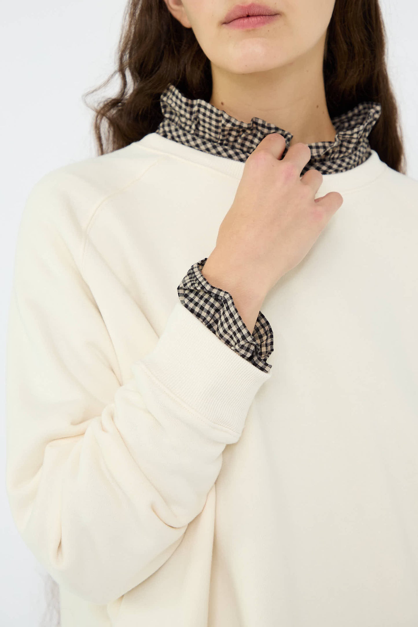 A person wearing Ichi Antiquités' French Terry Sweatshirt in Natural, made from 100% cotton, revealing a black and white checkered shirt underneath, holds the collar with one hand.