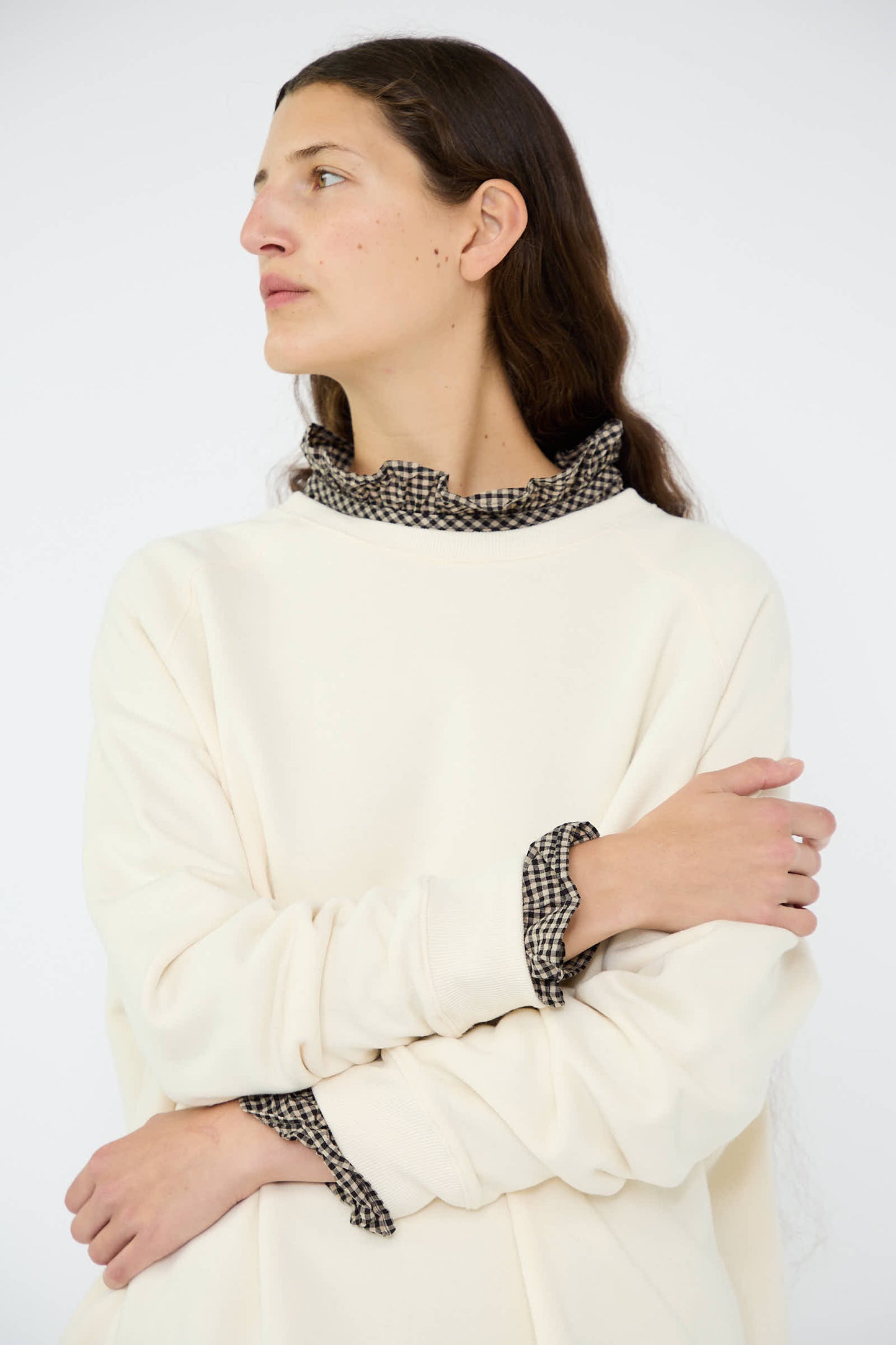 An individual with long hair is gazing to the side, dressed in a natural cream-colored French Terry Sweatshirt by Ichi Antiquités, crafted from 100% cotton and showcasing a checked ruffled neck and cuffs.