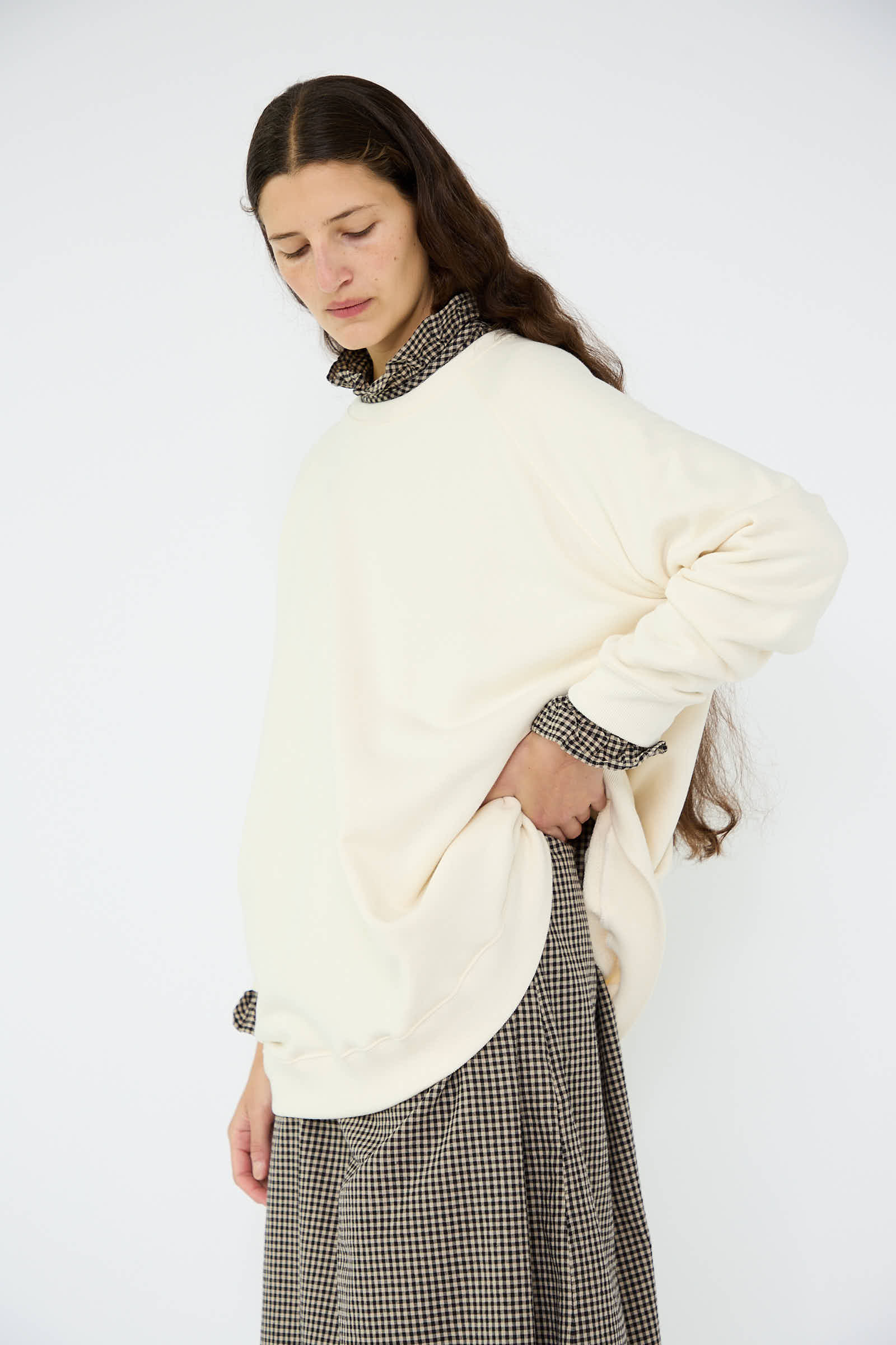 An individual donned an oversized French Terry Sweatshirt in Natural by Ichi Antiquités over a checkered shirt and skirt, posing against a white background.