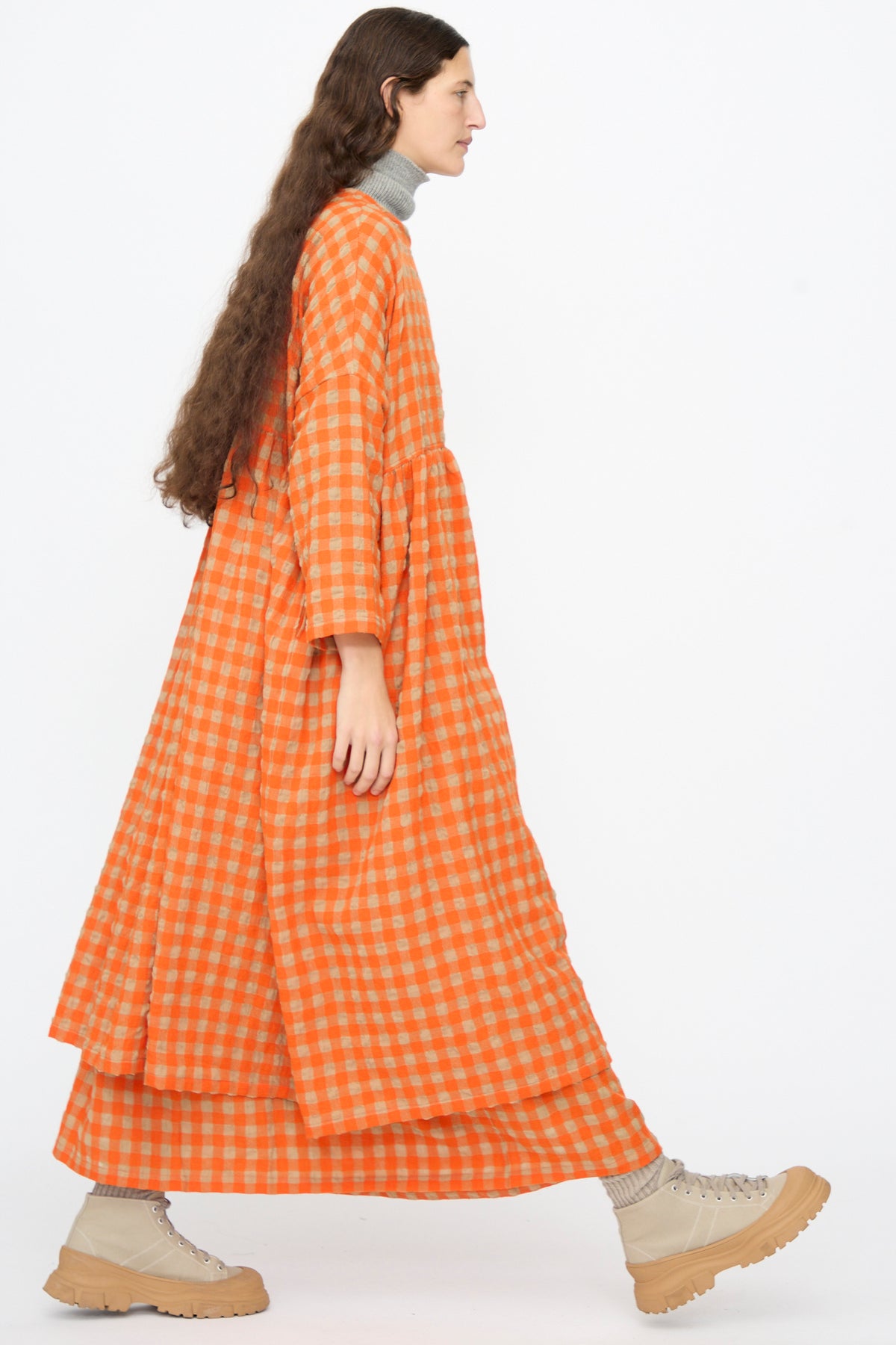 A person wearing an Ichi Antiquités Gingham Check Dress in Beige and Orange, styled with a tiered skirt over a grey turtleneck and beige high-top sneakers.
