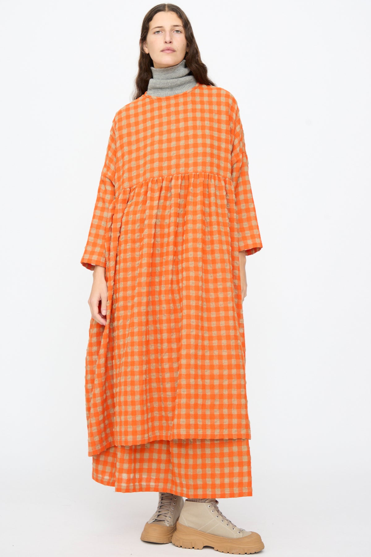 A person wearing an Ichi Antiquités Gingham Check Dress in Beige and Orange, layered over a grey turtleneck with beige high-top sneakers.
