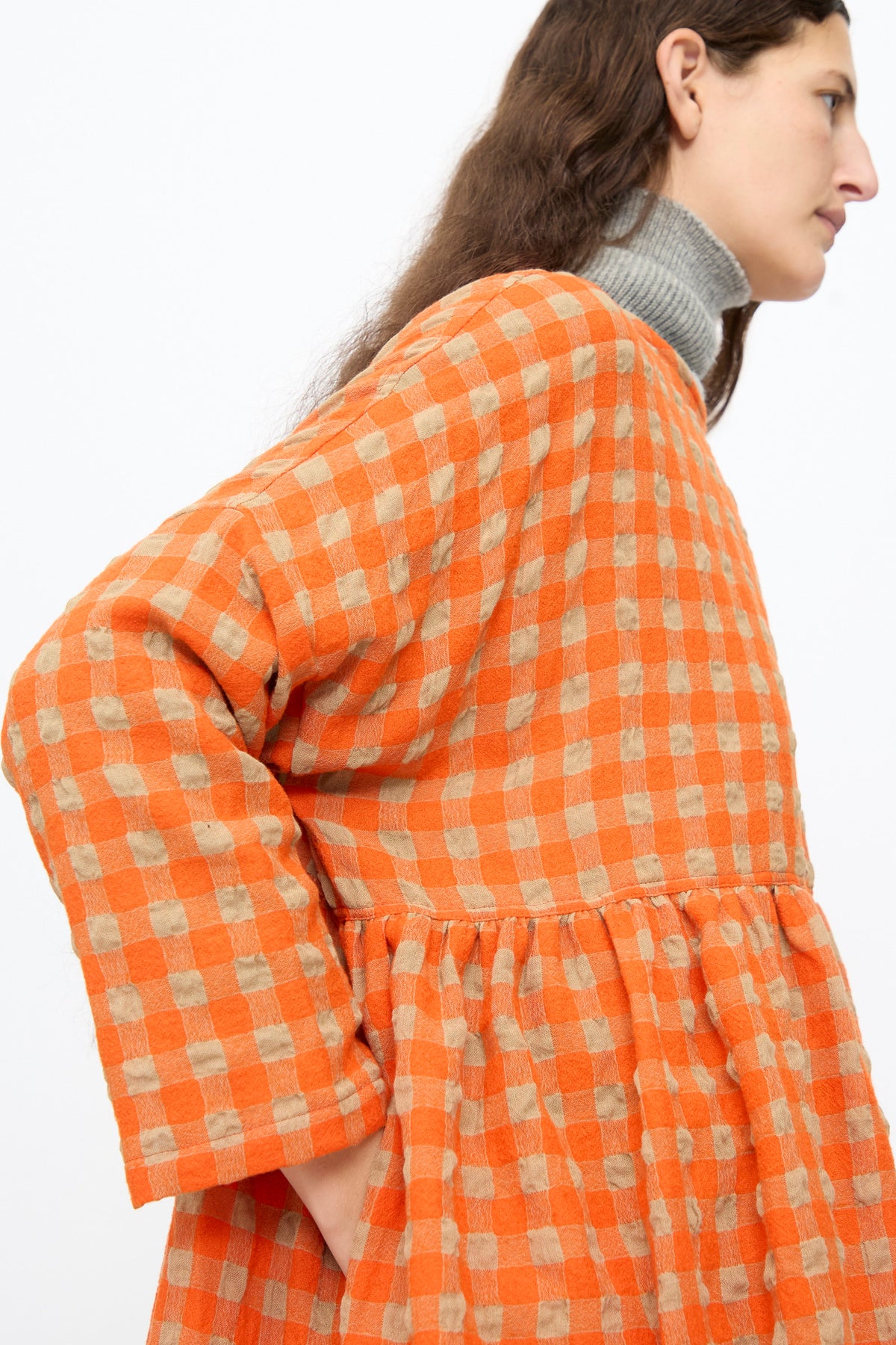 A person wearing an Ichi Antiquités Gingham Check Dress in Beige and Orange, featuring a long-sleeve, dropped-waist design layered over a grey turtleneck.