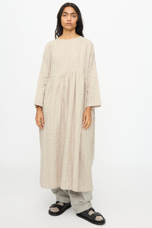 A person faces forward wearing the Ichi Antiquités Gingham Check Dress in Natural over light pants with black sandals, standing against a plain white background.