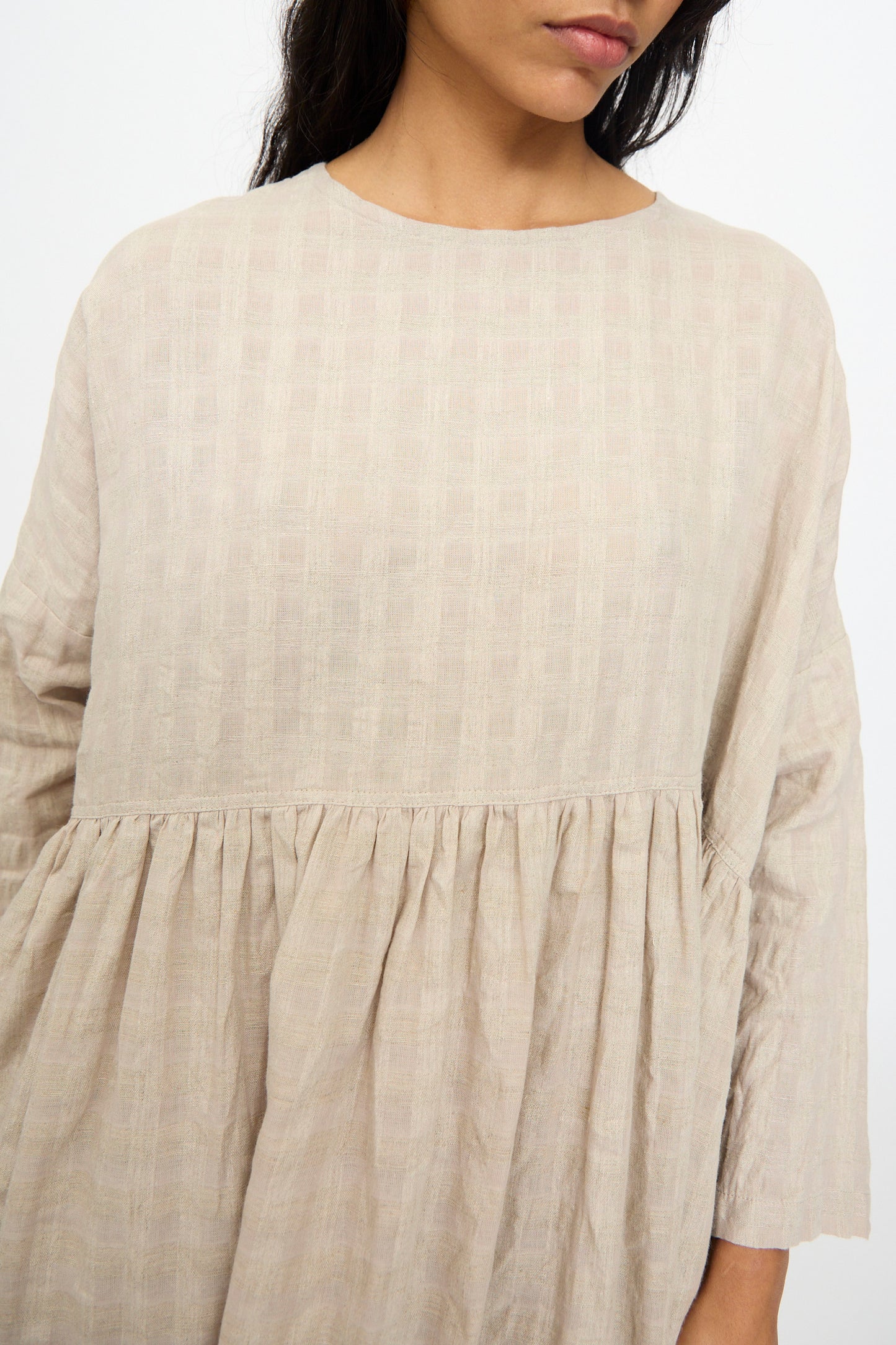 A woman models the Ichi Antiquités Gingham Check Dress in Natural, a loose-fitting, long sleeve cotton-linen blend with gathered waist detail, shown from shoulders to mid-thigh.