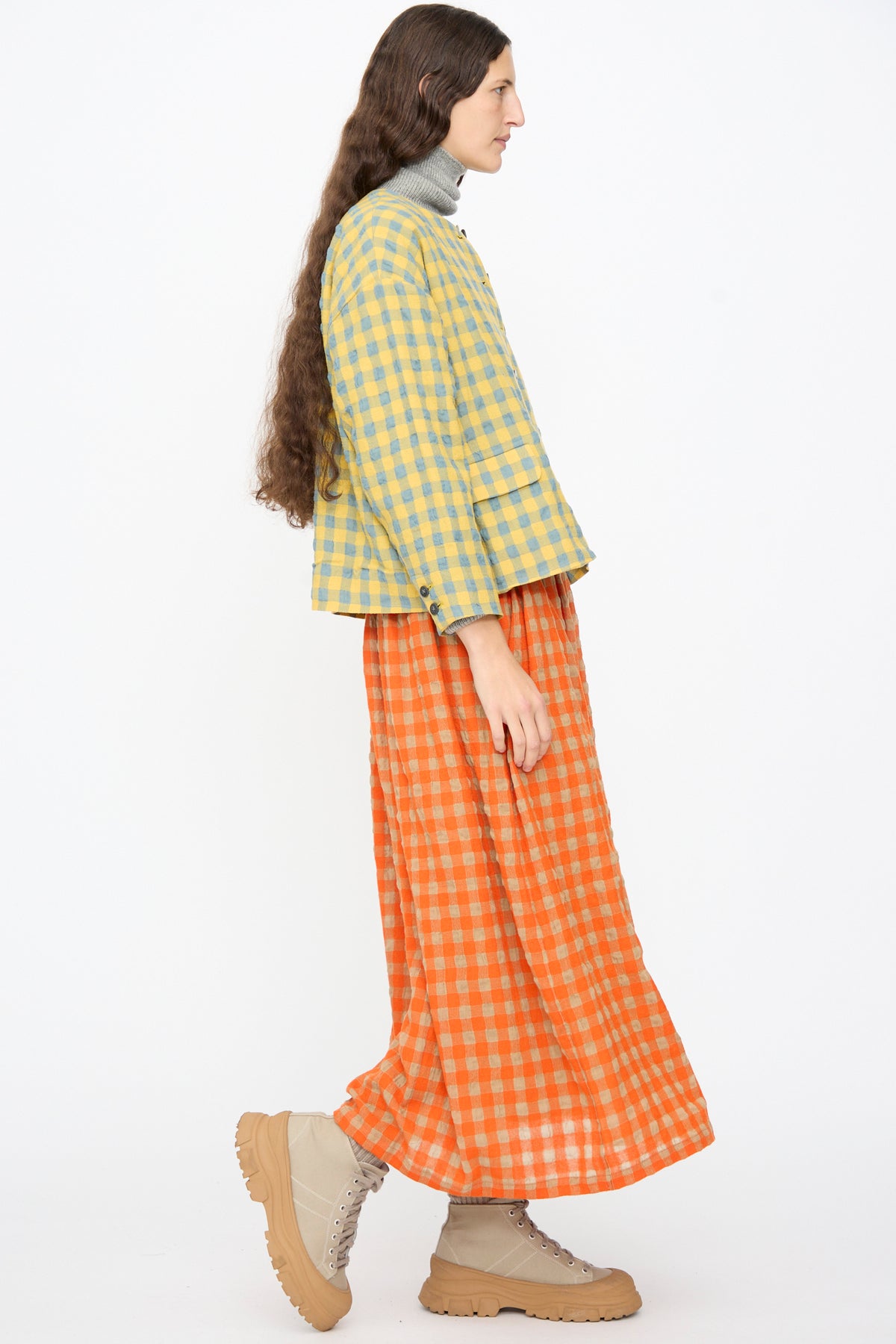 A person wears an Ichi Antiquités Gingham Check Jacket in Blue and Yellow over a grey turtleneck, an orange gingham skirt, and tan lace-up boots.