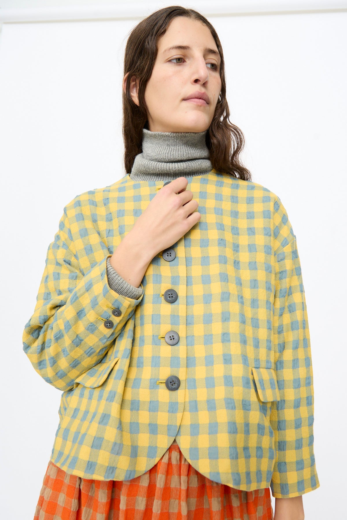A model wears an Ichi Antiquités Gingham Check Jacket in Blue and Yellow over a grey turtleneck and an orange plaid skirt.