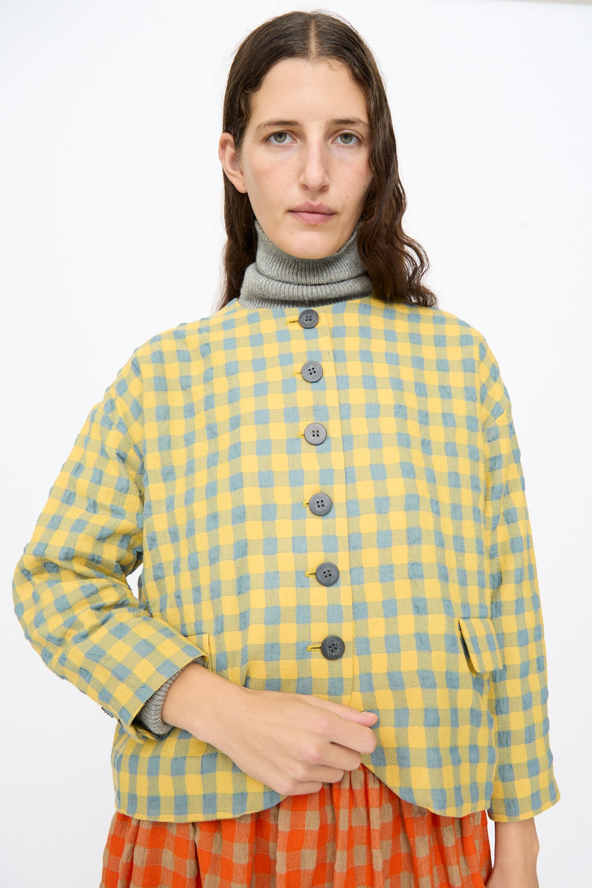 A person wearing an Ichi Antiquités Gingham Check Jacket in Blue and Yellow, buttoned over a grey turtleneck sweater.