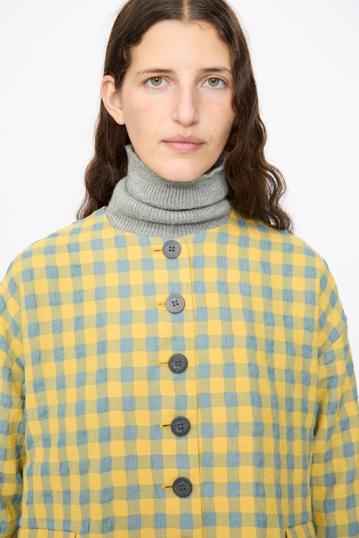A person wearing a blue and yellow Ichi Antiquités Gingham Check Jacket over a grey turtleneck sweater.
