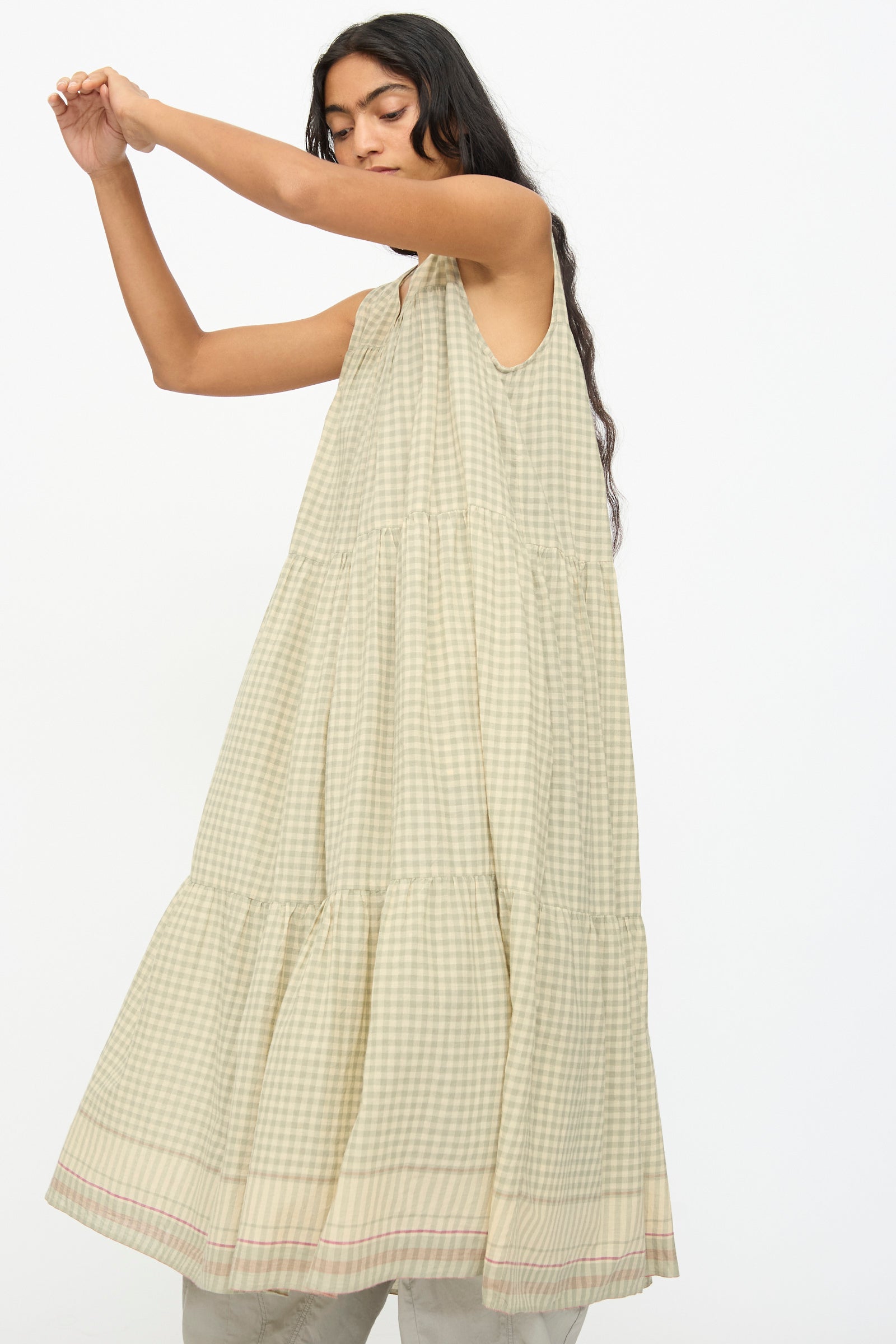 A woman poses against a plain backdrop in the Ichi Antiquités Gingham Check Khadi Cotton Dress in Khaki, featuring a relaxed fit and sleeveless design with a beige and white checkered pattern.