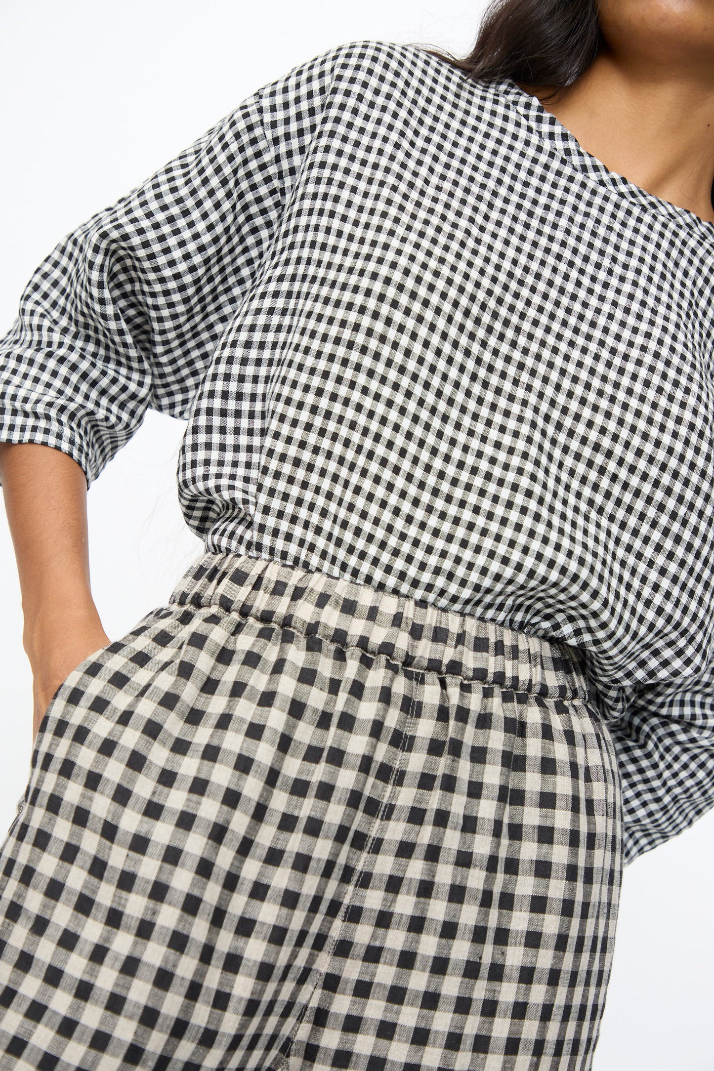 Model wears the Ichi Antiquités Gingham Check Pants in Natural and Black, featuring a high-waisted elastic waistband, paired with a black-and-white checkered long-sleeve top; photographed from shoulders to upper thighs against a plain background.