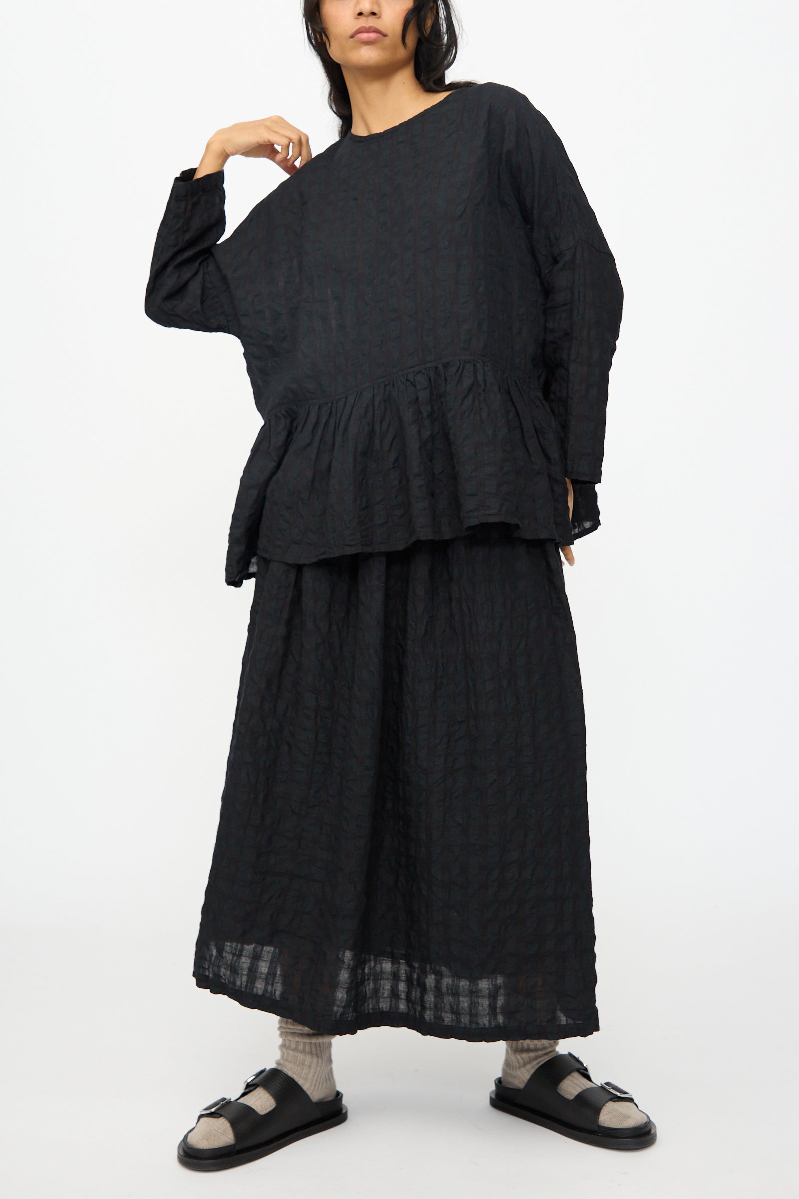 A person wears the Ichi Antiquités Gingham Check Pullover in Black with a matching black skirt, socks, and sandals, standing against a plain white background.