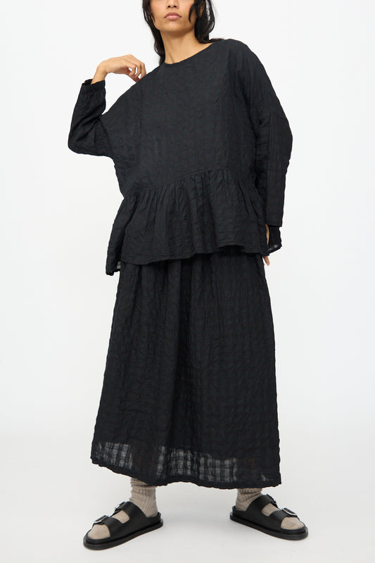 A person wears the Ichi Antiquités Gingham Check Pullover in Black with a matching black skirt, socks, and sandals, standing against a plain white background.