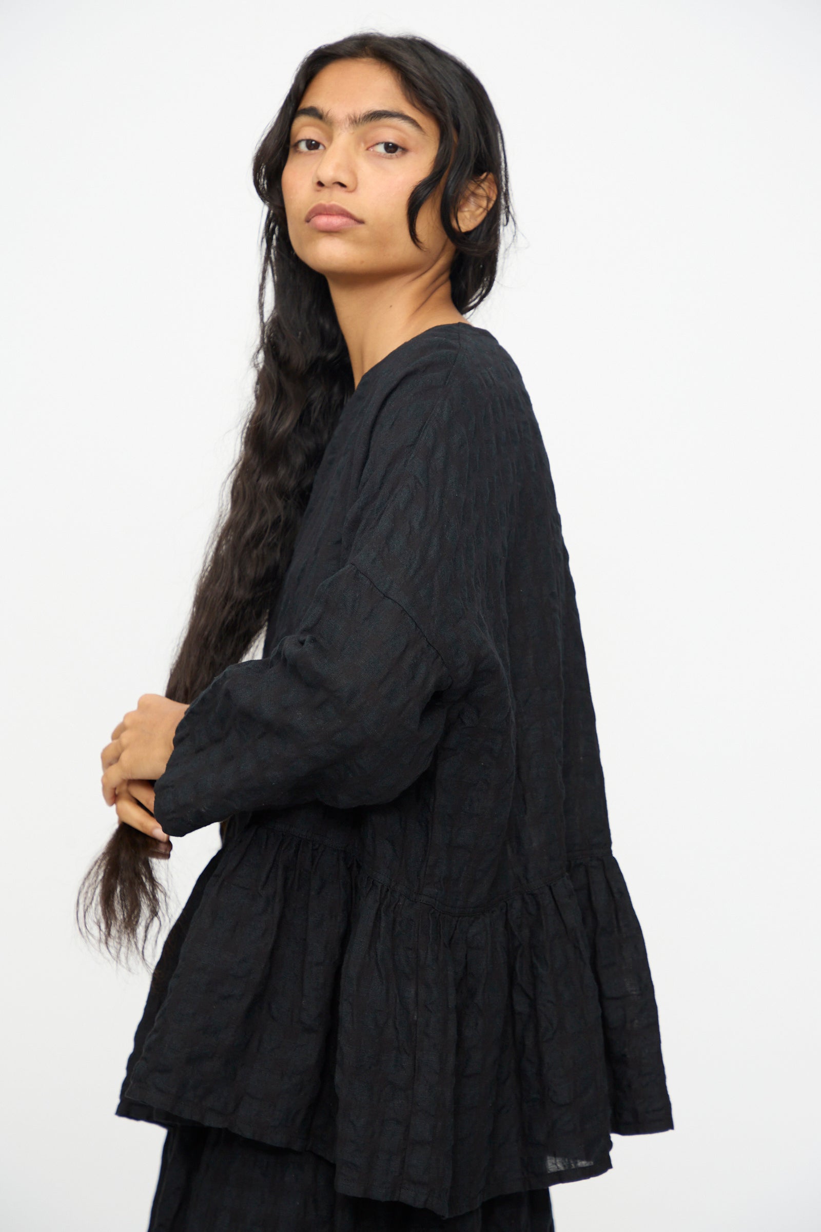A person with long dark hair, wearing the Ichi Antiquités Gingham Check Pullover in Black, stands against a plain white background, facing slightly to the side.