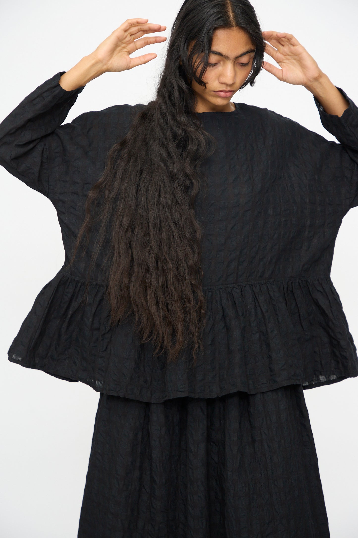 A person with long, wavy hair wears the Ichi Antiquités Gingham Check Pullover in Black, styled in a relaxed fit, standing against a plain white background.