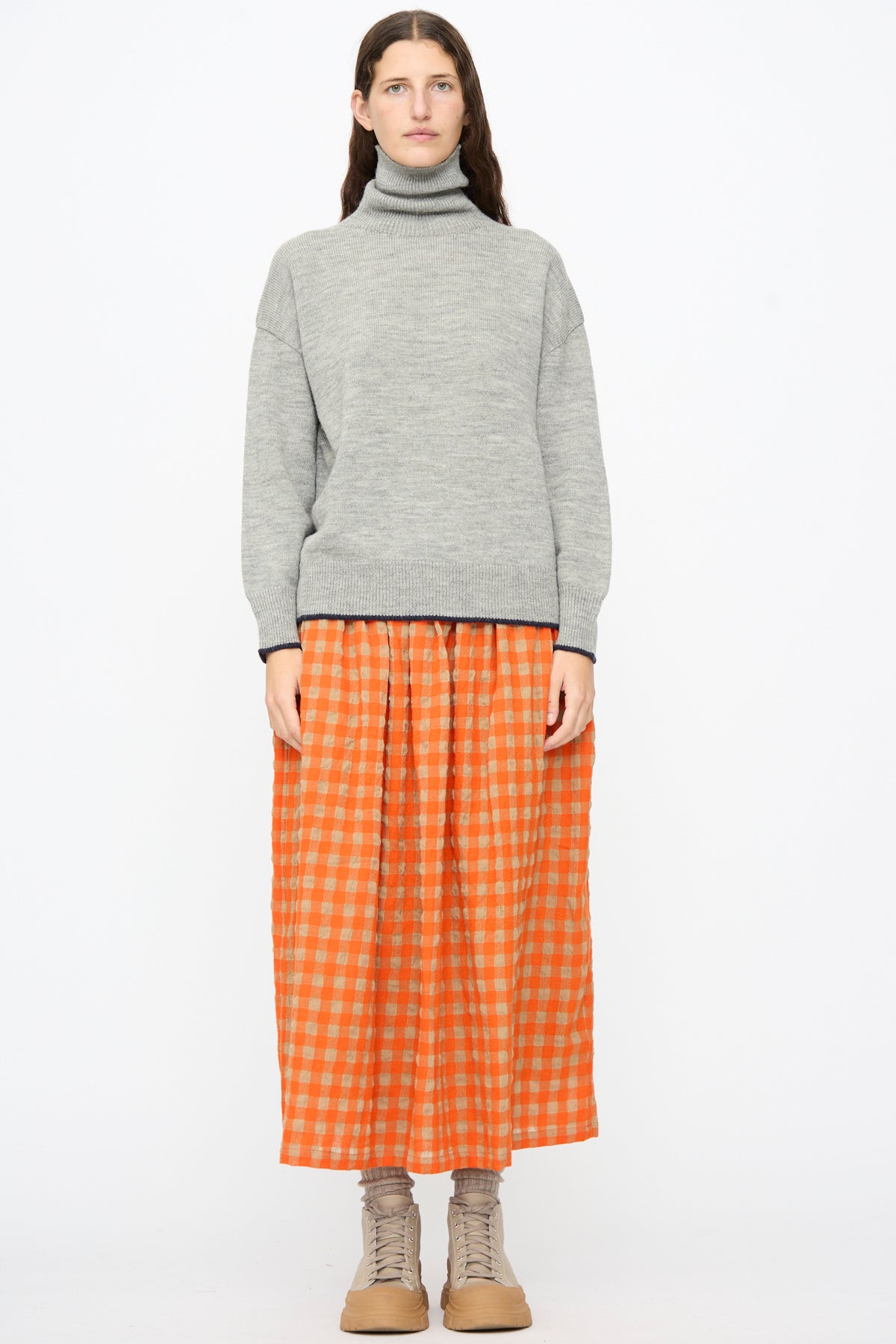 A person wearing a grey turtleneck sweater, an Ichi Antiquités Gingham Check Skirt in Beige and Orange, and beige lace-up boots.