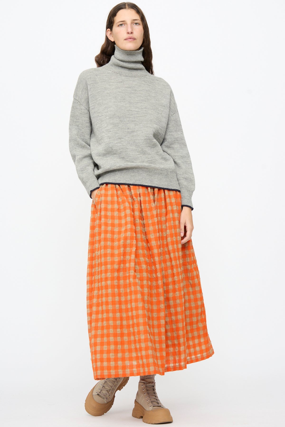 A person wears a grey turtleneck sweater, an Ichi Antiquités Gingham Check Skirt in Beige and Orange, and tan lace-up boots.