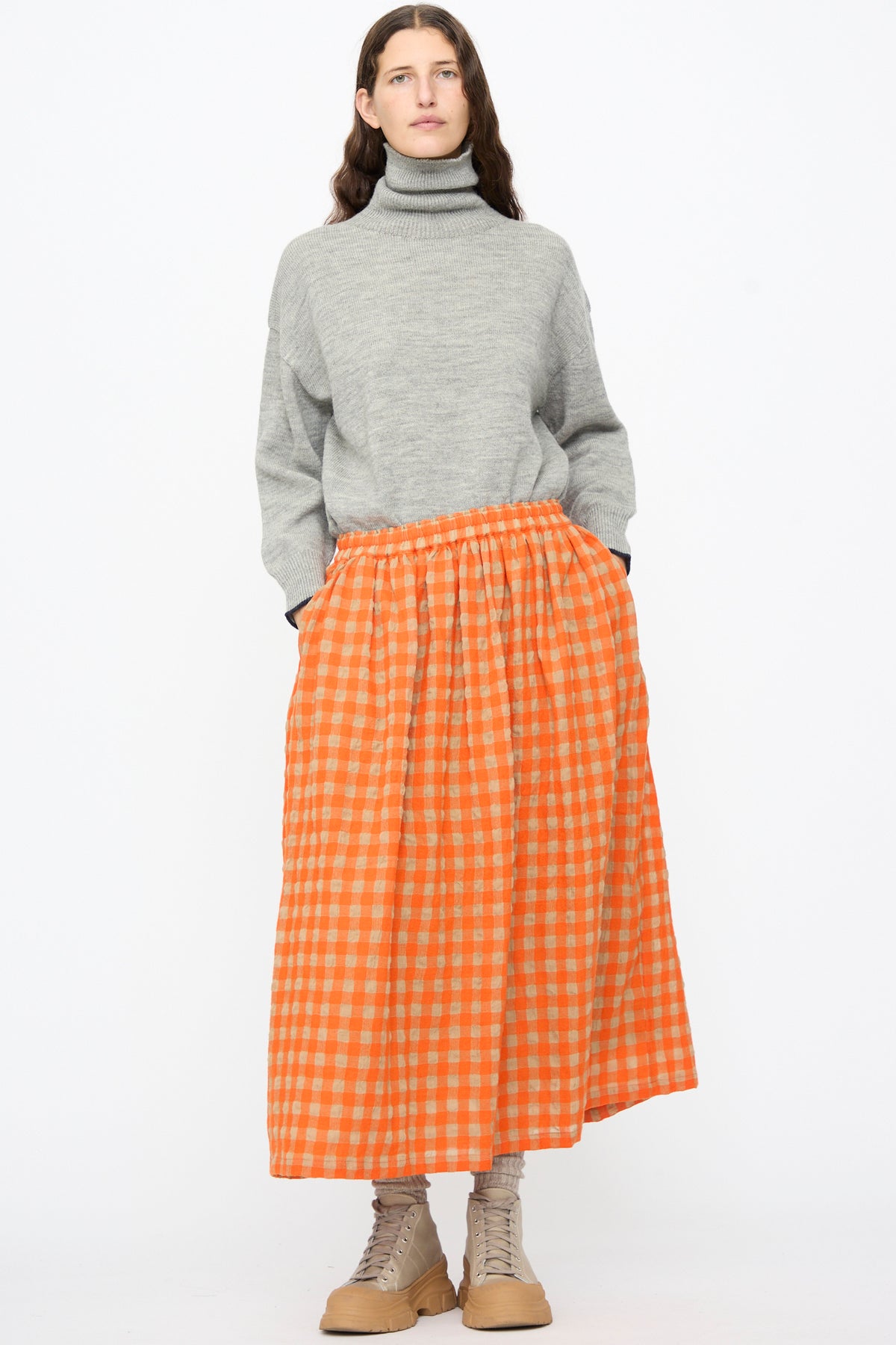 A person wearing a grey turtleneck sweater and an Ichi Antiquités Gingham Check Skirt in Beige and Orange, an orange and beige gingham-check A-line midi skirt.