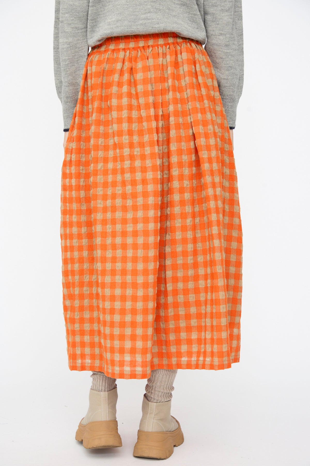 A person wearing an Ichi Antiquités Gingham Check Skirt in Beige and Orange with a grey sweater and beige platform boots.