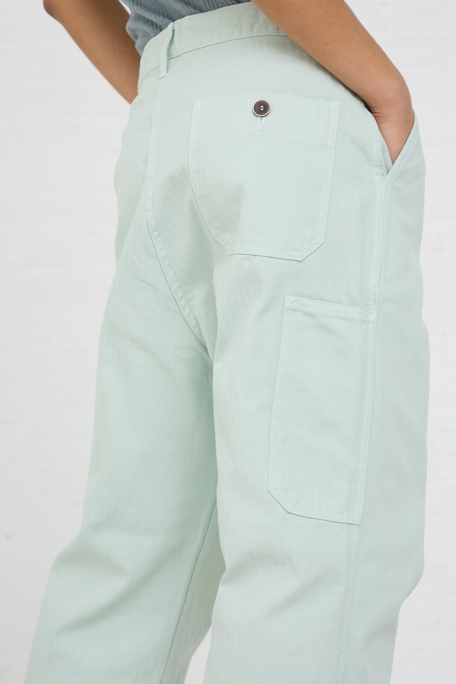 Person wearing Ichi Antiquités Herringbone Garment Dye Pant in Ice Green trousers with a close-up on the back pocket.